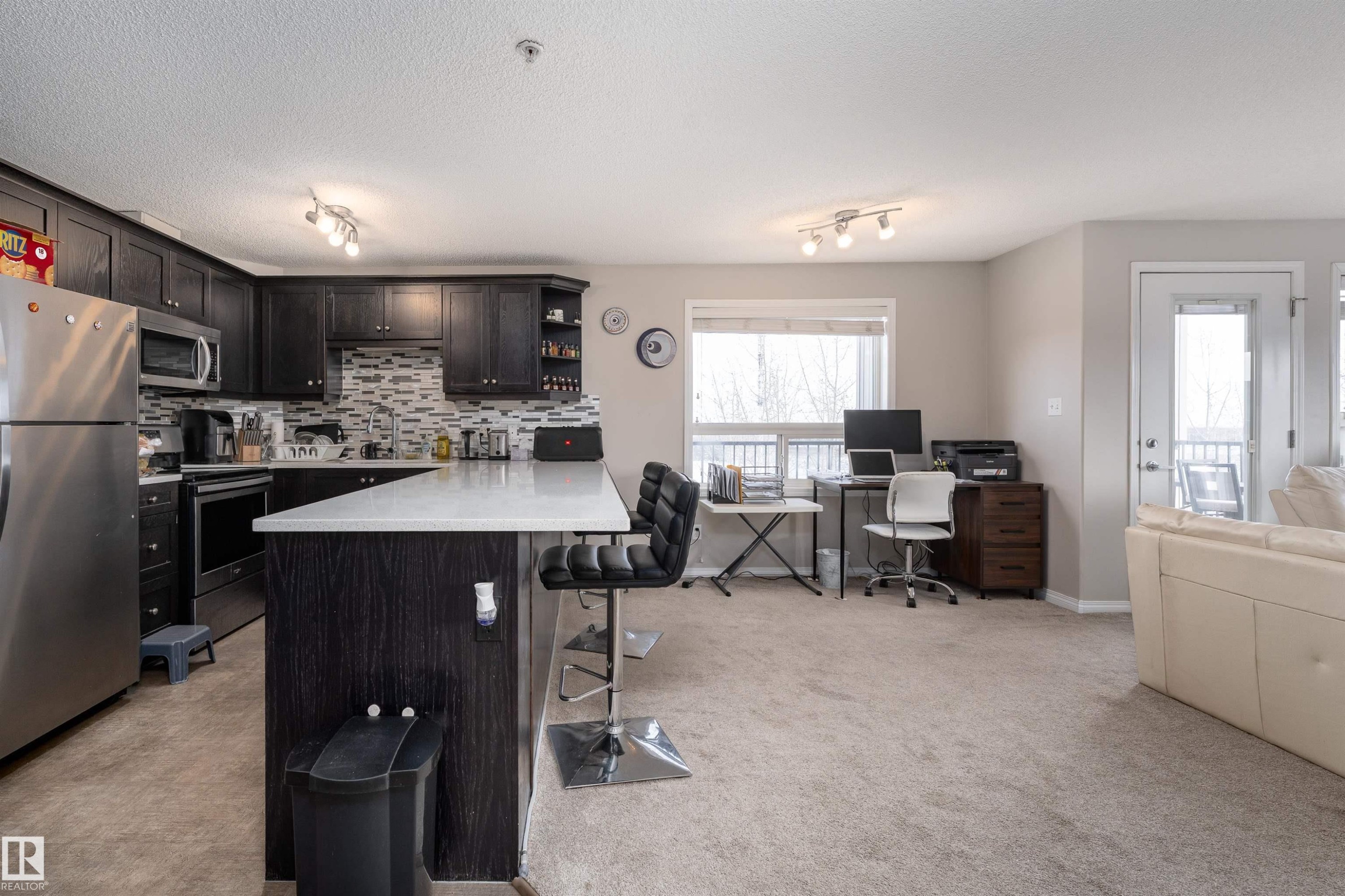 Kitchen featuring stainless steel appliances, open shelves, a kitchen bar, rail lighting, and a peninsula - 325 1520 Hammond Gate, Edmonton, AB - Indoor Photo Showing Kitchen With Stainless Steel Kitchen