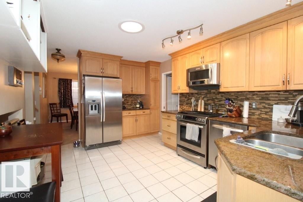 Kitchen featuring stainless steel appliances, light wood finish cabinets, dark stone countertops, and light tile patterned floors - 2812 35 Street Nw, Edmonton, AB - Indoor Photo Showing Kitchen With Double Sink