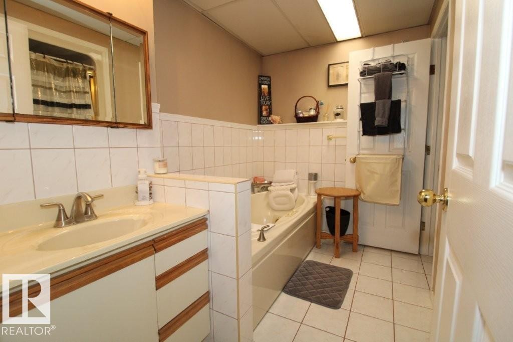 Full bathroom with curtained shower, vanity, tile walls, light tile patterned floors, and a bath - 2812 35 Street Nw, Edmonton, AB - Indoor Photo Showing Bathroom