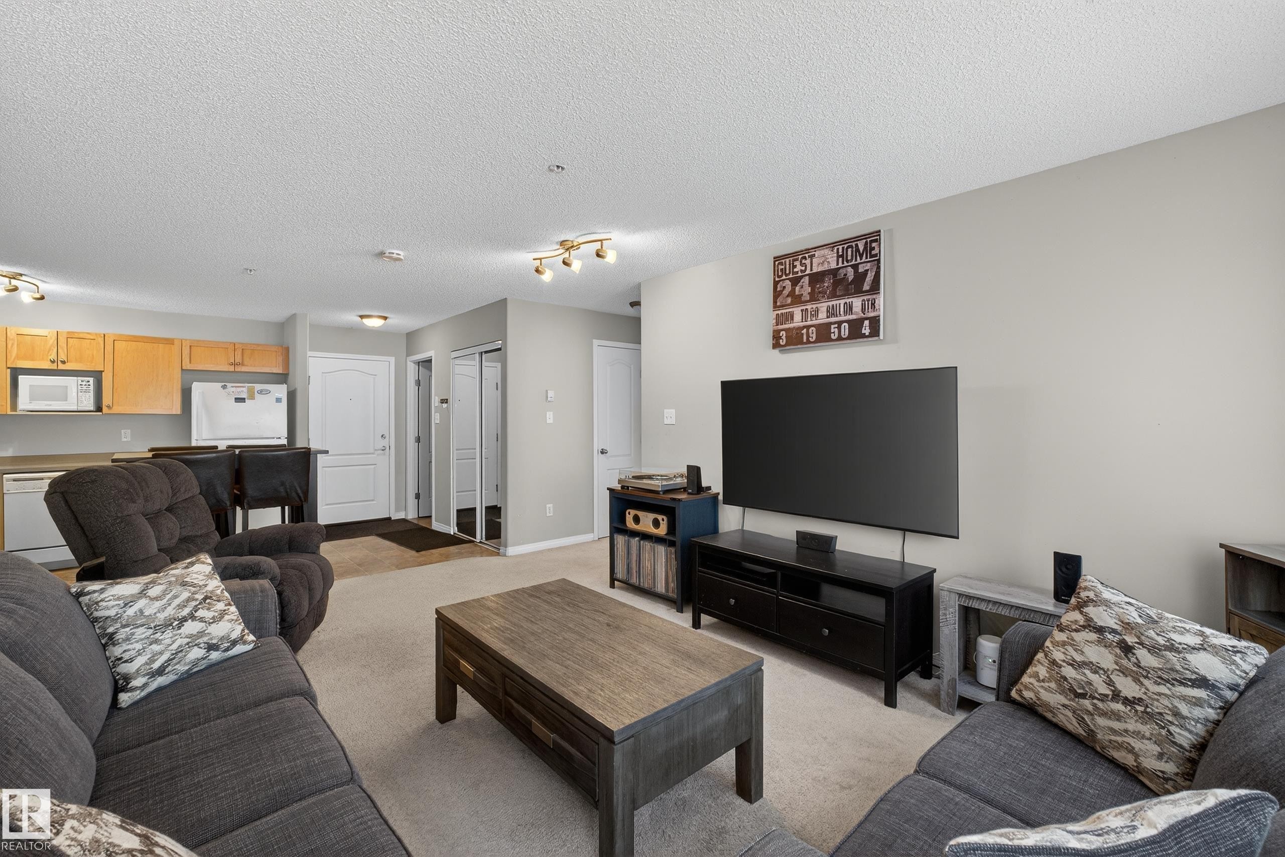 Living area featuring light colored carpet and a textured ceiling - 131 1520 Hammond Gate, Edmonton, AB - Indoor Photo Showing Living Room