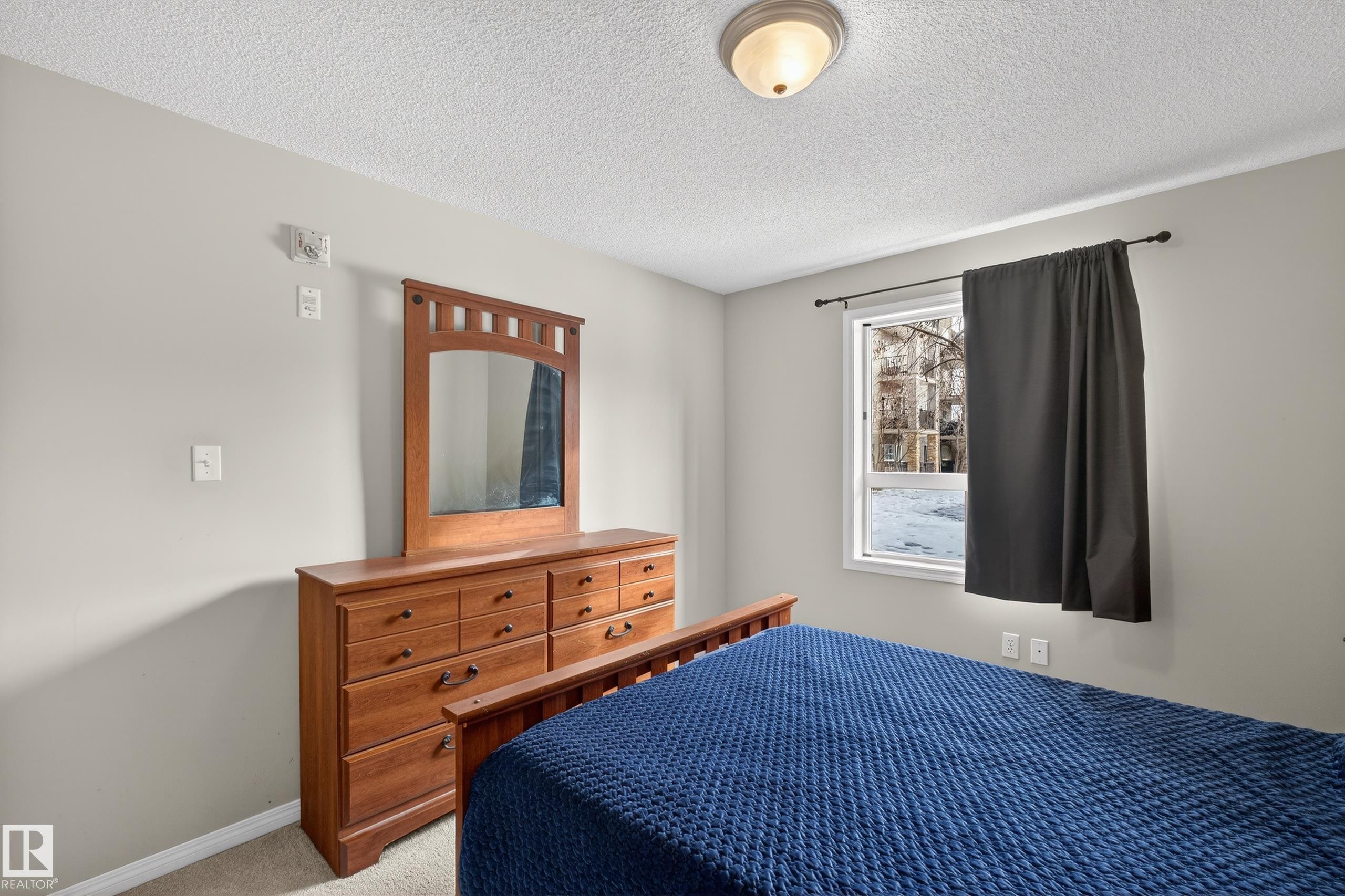 Carpeted bedroom featuring a textured ceiling and baseboards - 131 1520 Hammond Gate, Edmonton, AB - Indoor Photo Showing Bedroom