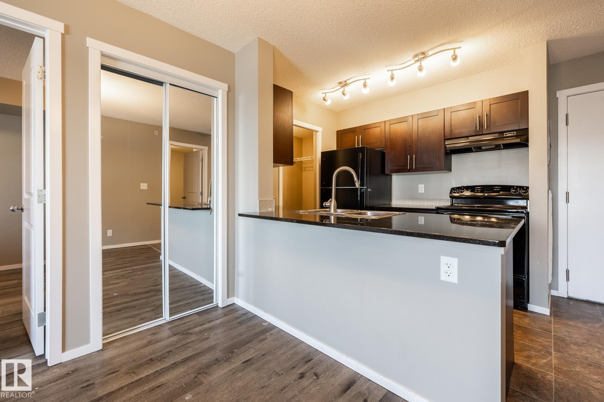 Kitchen with range with electric cooktop, dark stone counters, a peninsula, freestanding refrigerator, and a textured ceiling - 433 3315 James Mowatt Trail, Edmonton, AB - Indoor Photo Showing Kitchen