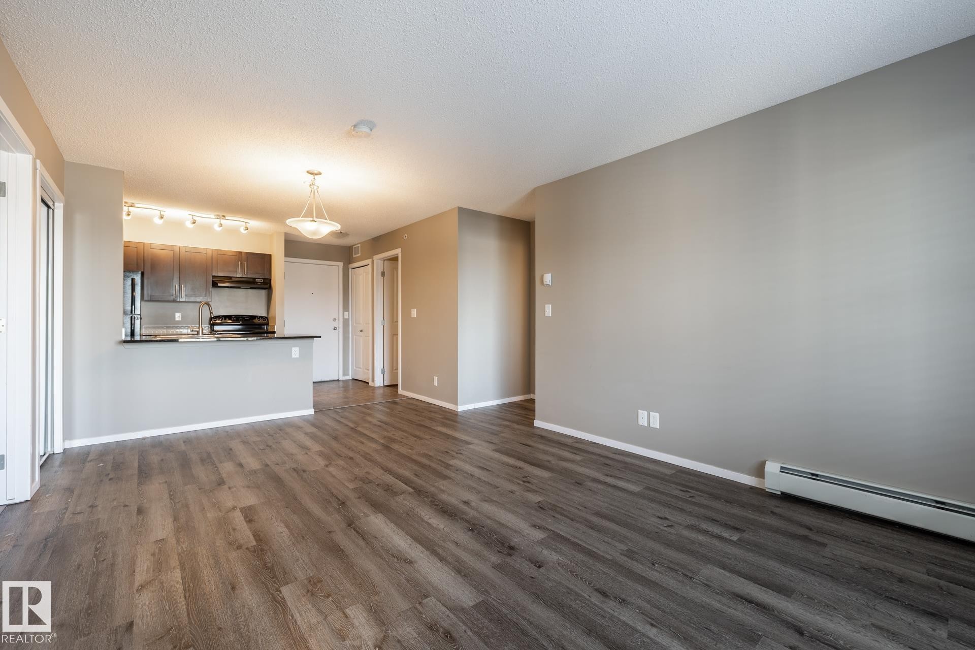 Unfurnished living room with dark wood finished floors, a textured ceiling, and a baseboard heating unit - 433 3315 James Mowatt Trail, Edmonton, AB - Indoor