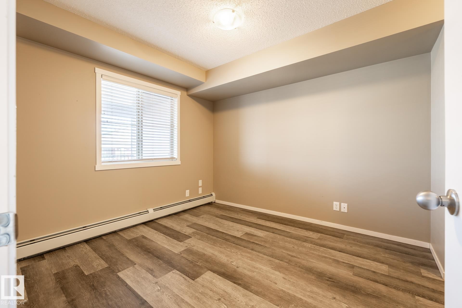 Empty room featuring baseboard heating, a textured ceiling, and wood finished floors - 433 3315 James Mowatt Trail, Edmonton, AB - Indoor Photo Showing Other Room