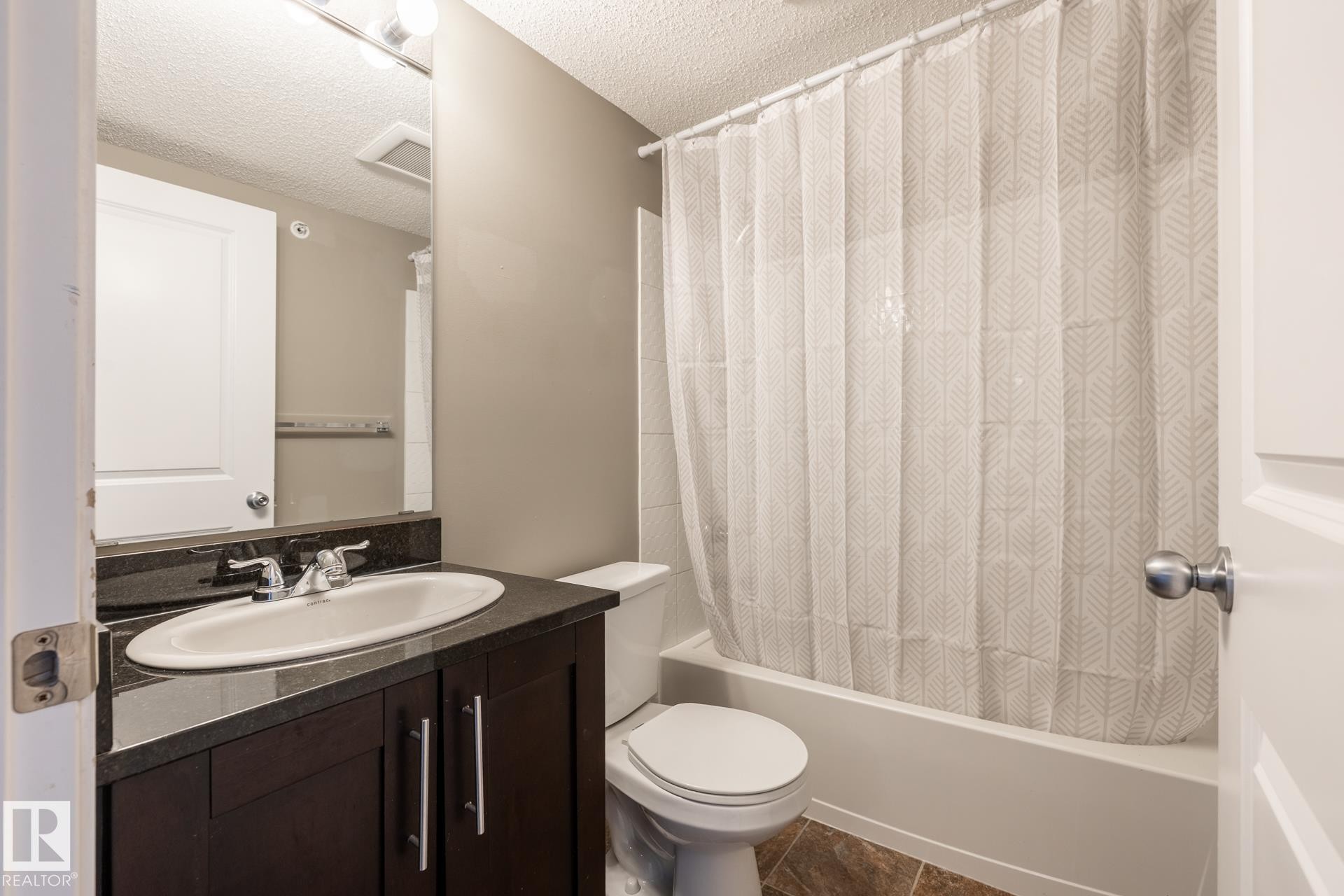 Bathroom with a textured ceiling, vanity, and shower / tub combo with curtain - 433 3315 James Mowatt Trail, Edmonton, AB - Indoor Photo Showing Bathroom