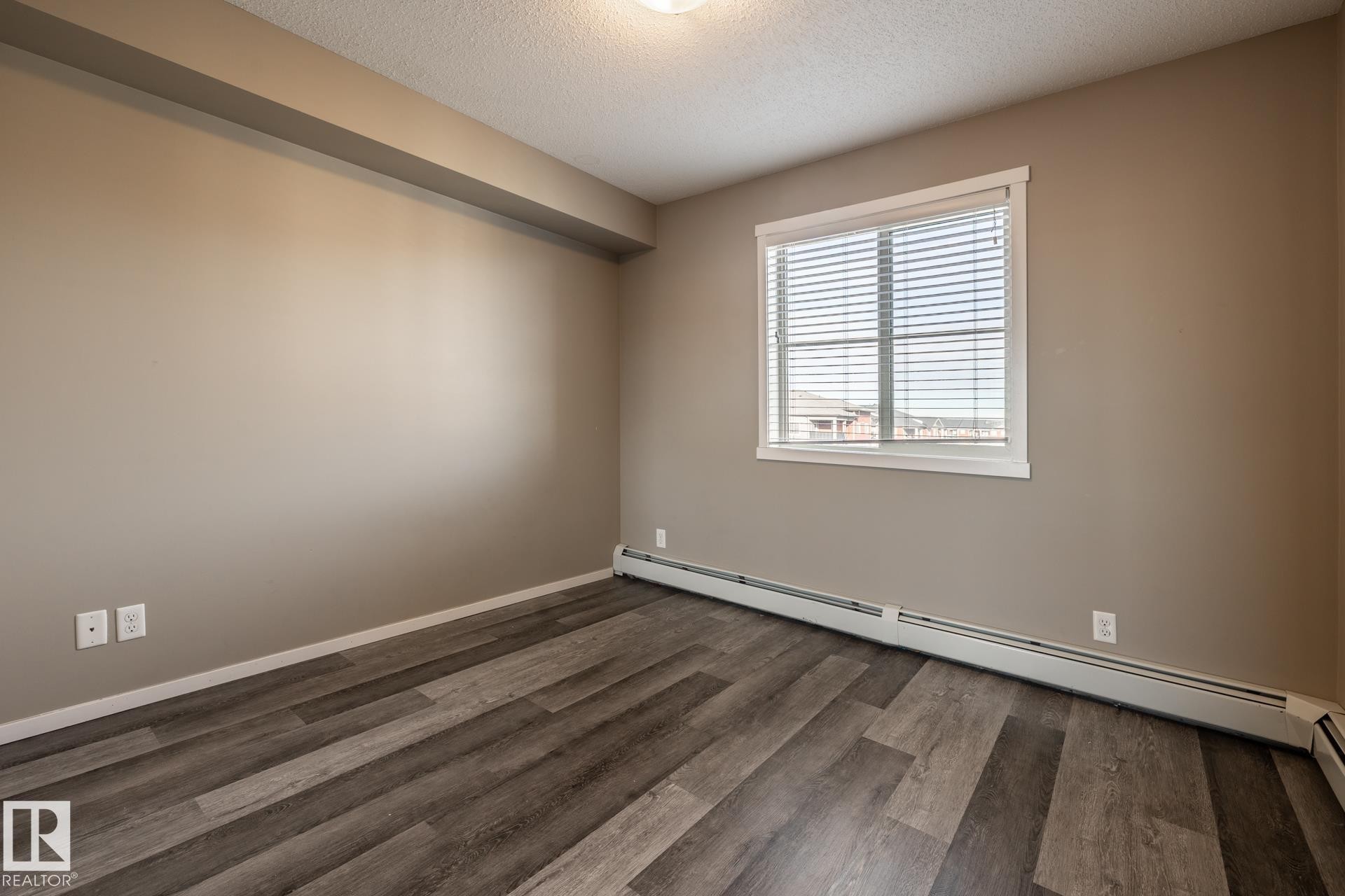 Unfurnished room with baseboard heating, a textured ceiling, and dark wood-style flooring - 433 3315 James Mowatt Trail, Edmonton, AB - Indoor Photo Showing Other Room