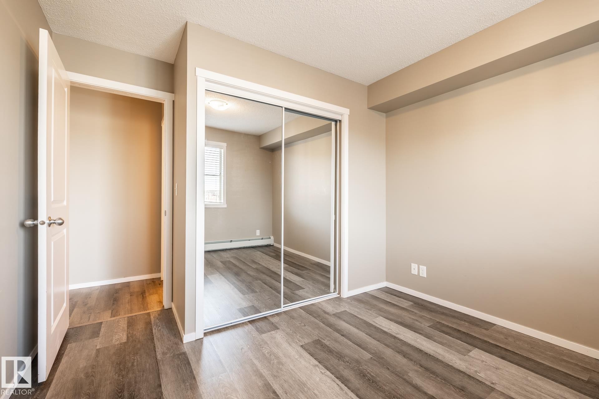 Unfurnished bedroom with a textured ceiling, dark wood finished floors, a closet, and a baseboard radiator - 433 3315 James Mowatt Trail, Edmonton, AB - Indoor Photo Showing Other Room