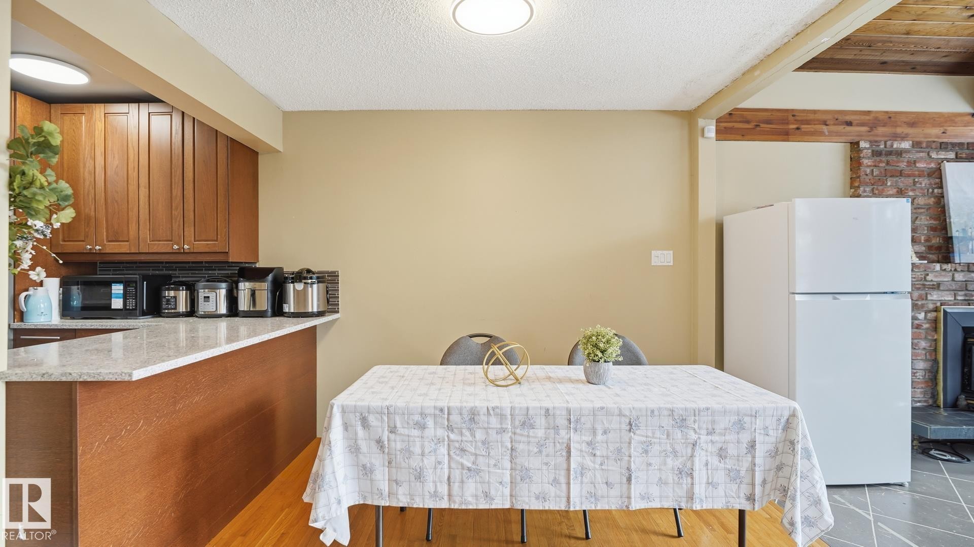 Kitchen featuring freestanding refrigerator, wood finish cabinets, light stone counters, a textured ceiling, and black microwave - 11520 78 Avenue Nw, Edmonton, AB - Indoor Photo Showing Kitchen