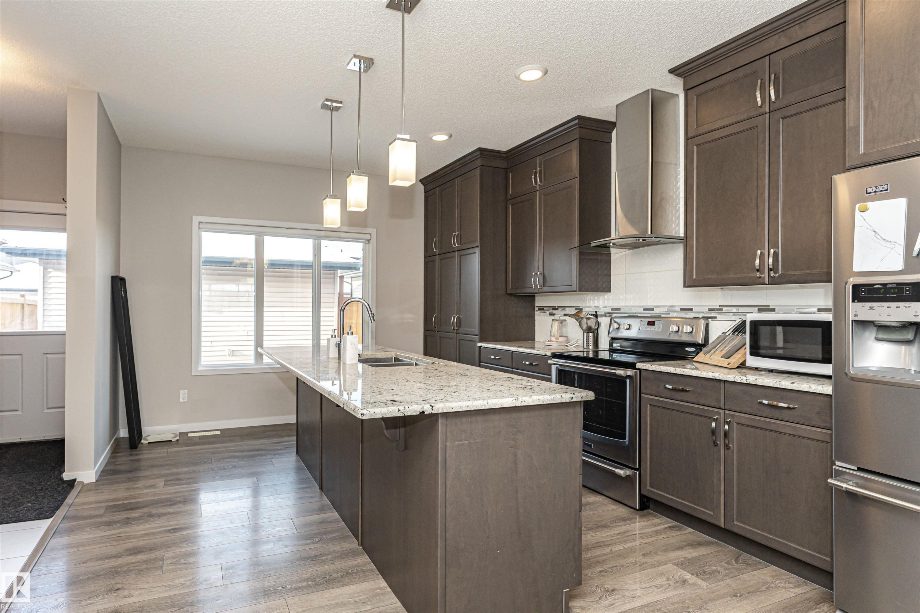 Kitchen with stainless steel appliances, dark wood finish cabinets, light stone countertops, a breakfast bar area, and light wood-style floors - 4008 Allan Crescent, Edmonton, AB - Indoor Photo Showing Kitchen With Upgraded Kitchen