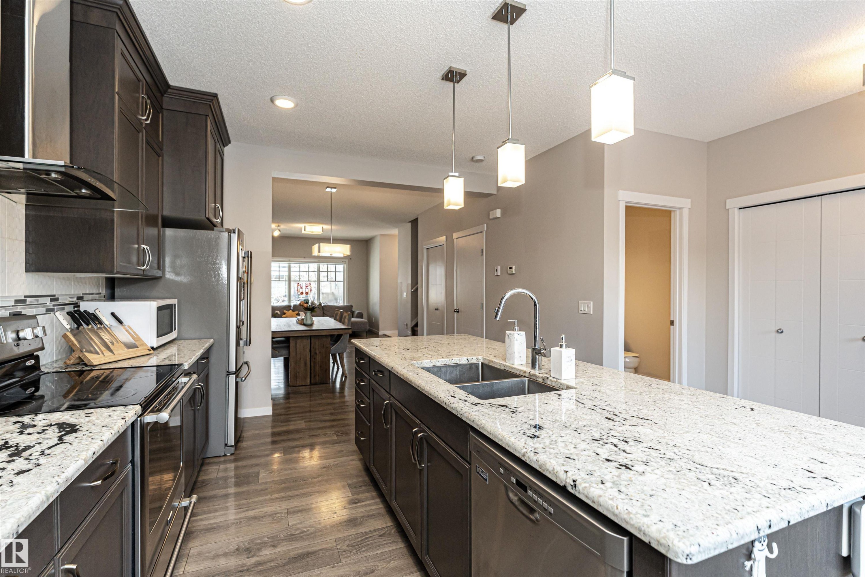 Kitchen with stainless steel appliances, decorative light fixtures, light stone counters, dark wood finish cabinetry, and a textured ceiling - 4008 Allan Crescent, Edmonton, AB - Indoor Photo Showing Kitchen With Stainless Steel Kitchen With Double Sink With Upgraded Kitchen