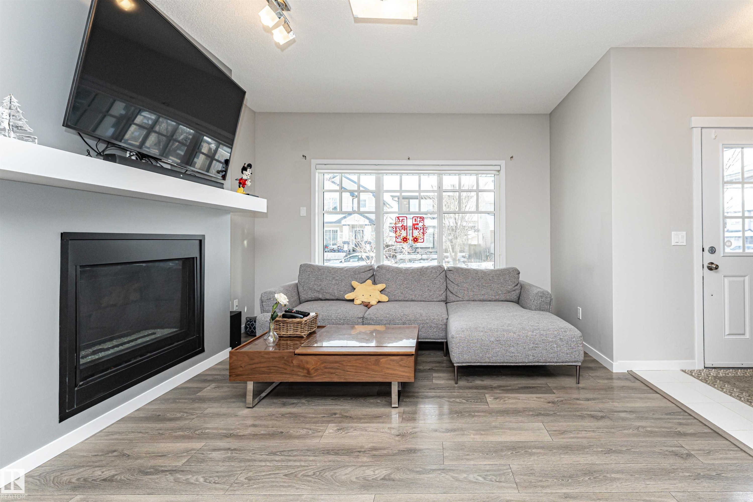 Living area featuring light wood-type flooring, a glass covered fireplace, and rail lighting - 4008 Allan Crescent, Edmonton, AB - Indoor Photo Showing Living Room With Fireplace