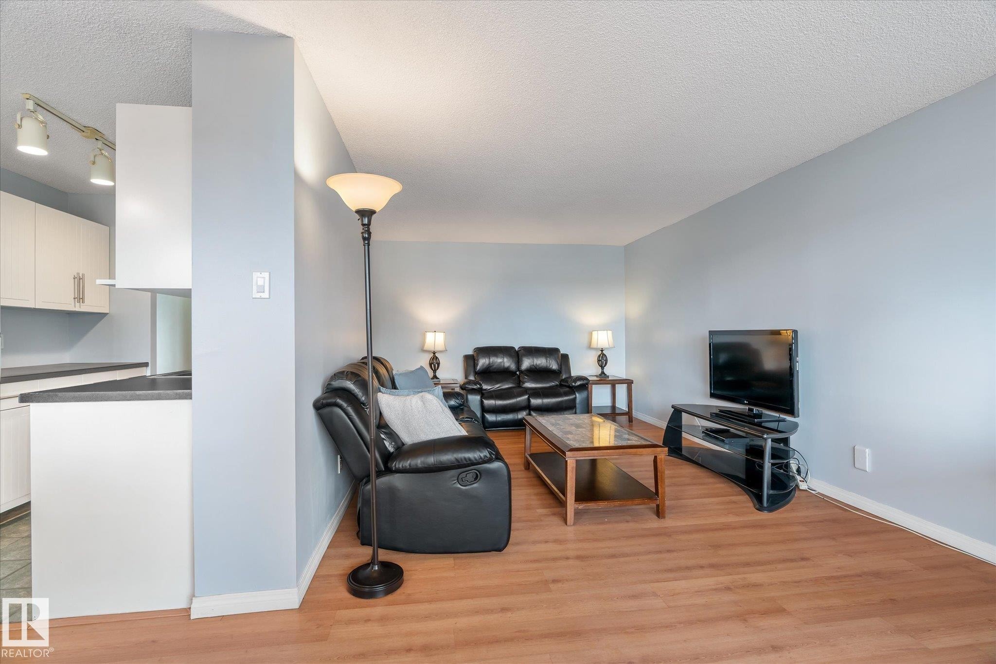 Living room featuring a textured ceiling, light wood finished floors, and rail lighting - 304 9725 106 Street, Edmonton, AB - Indoor Photo Showing Living Room