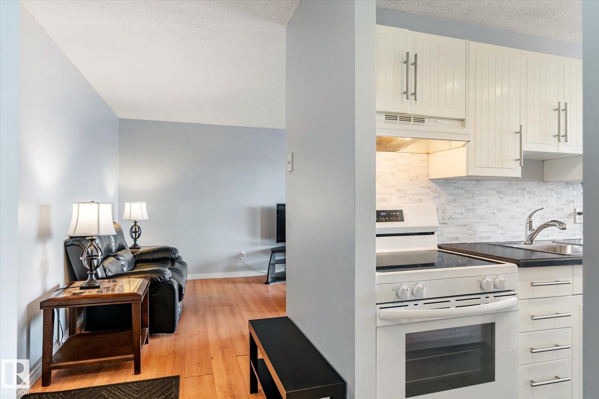 Kitchen with white electric stove, dark countertops, a textured ceiling, light wood-style floors, and backsplash - 304 9725 106 Street, Edmonton, AB - Indoor Photo Showing Kitchen