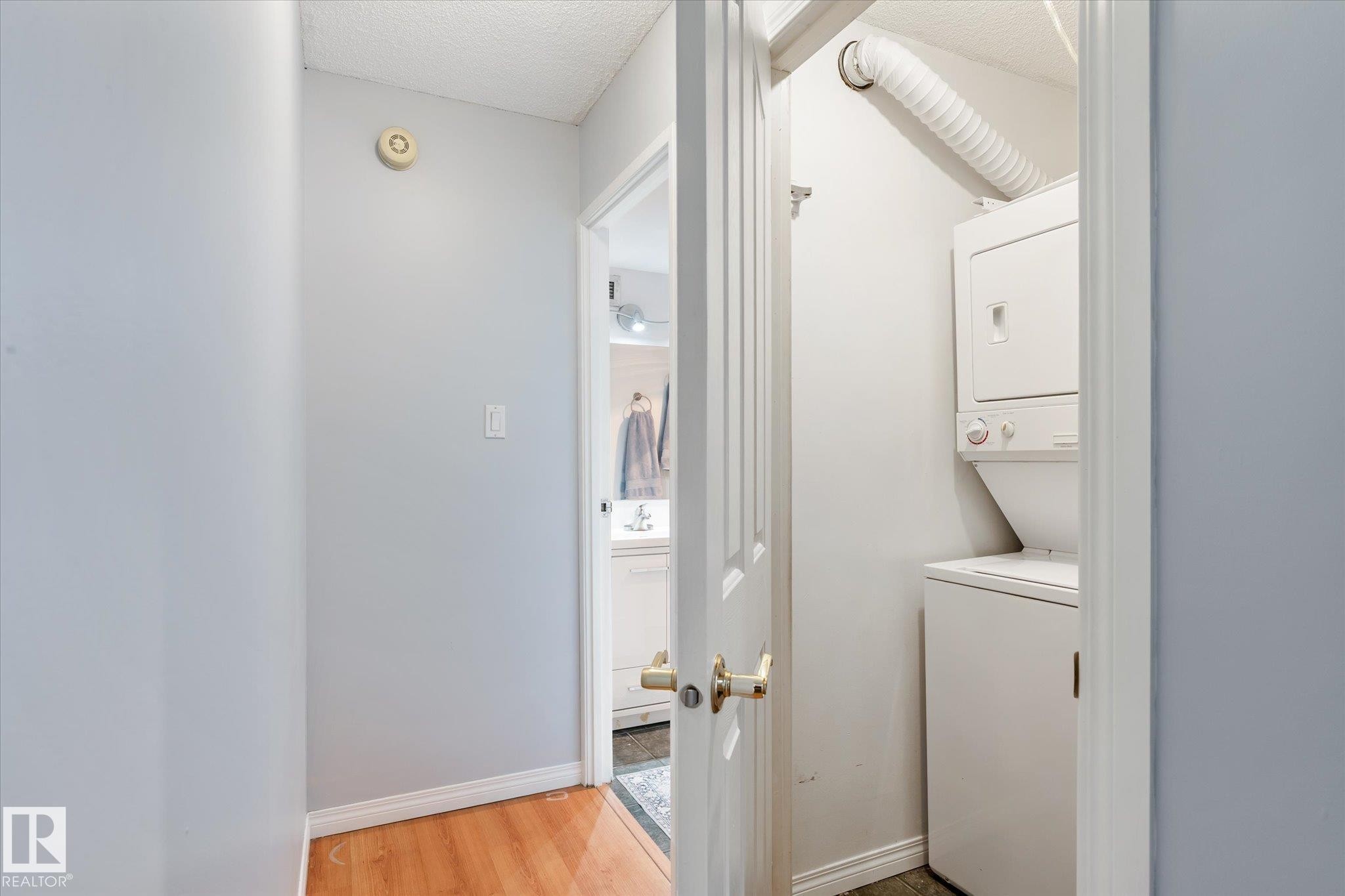 Laundry room with light wood-style floors, stacked washer / drying machine, and a textured ceiling - 304 9725 106 Street, Edmonton, AB - Indoor Photo Showing Laundry Room