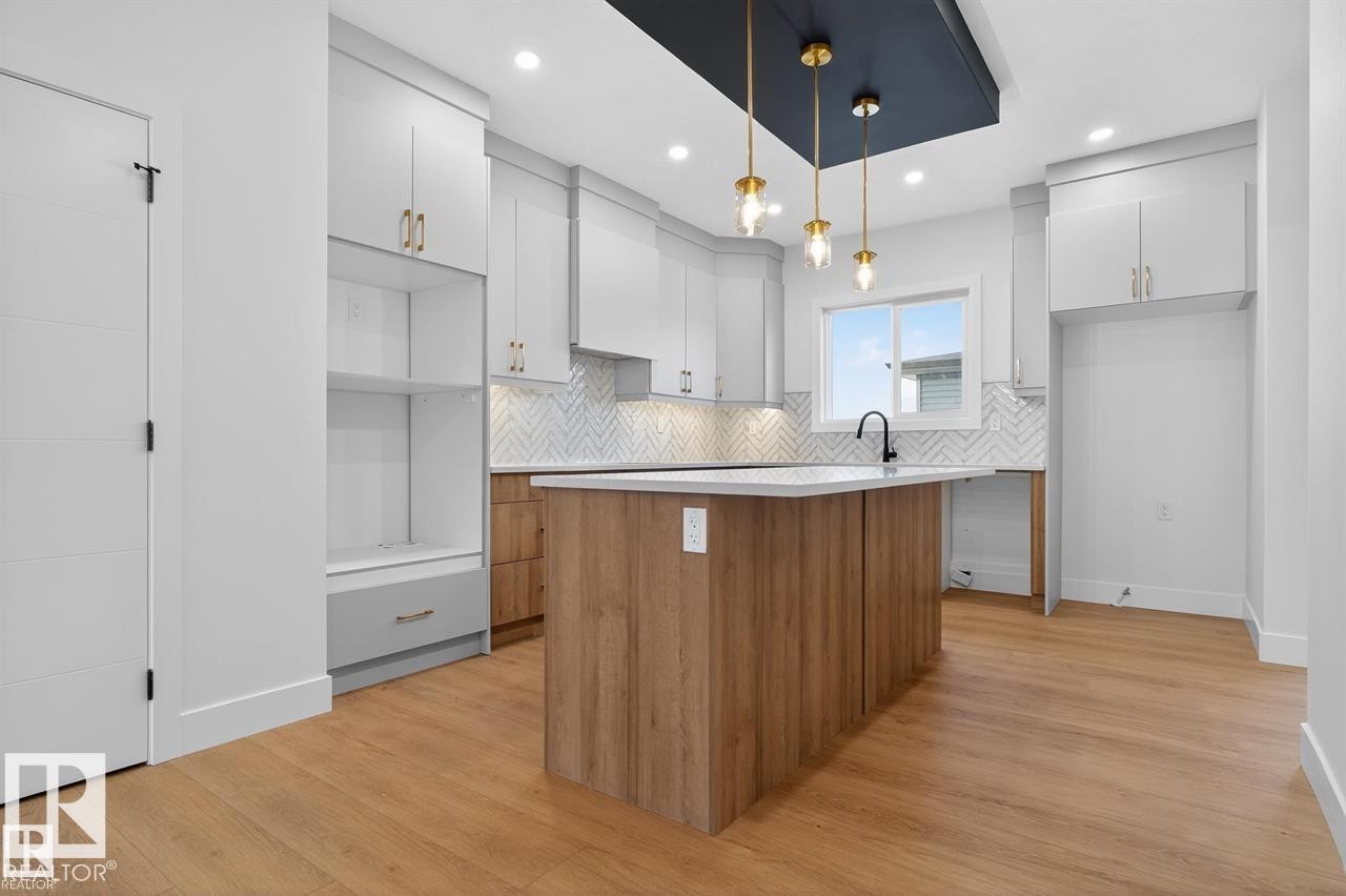 Two tone kitchen with two tone color scheme, light wood-style flooring, a kitchen island, hanging light fixtures, and tasteful backsplash - 47 River Birch Way, St. Albert, AB - Indoor Photo Showing Kitchen