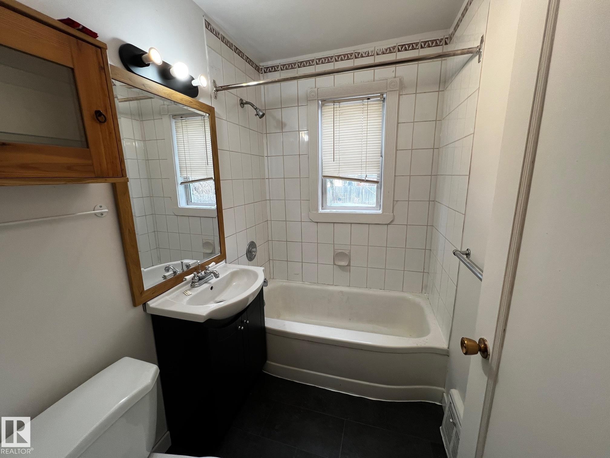 Bathroom featuring washtub / shower combination, vanity, and dark tile patterned floors - 10830 68 Avenue, Edmonton, AB - Indoor Photo Showing Bathroom