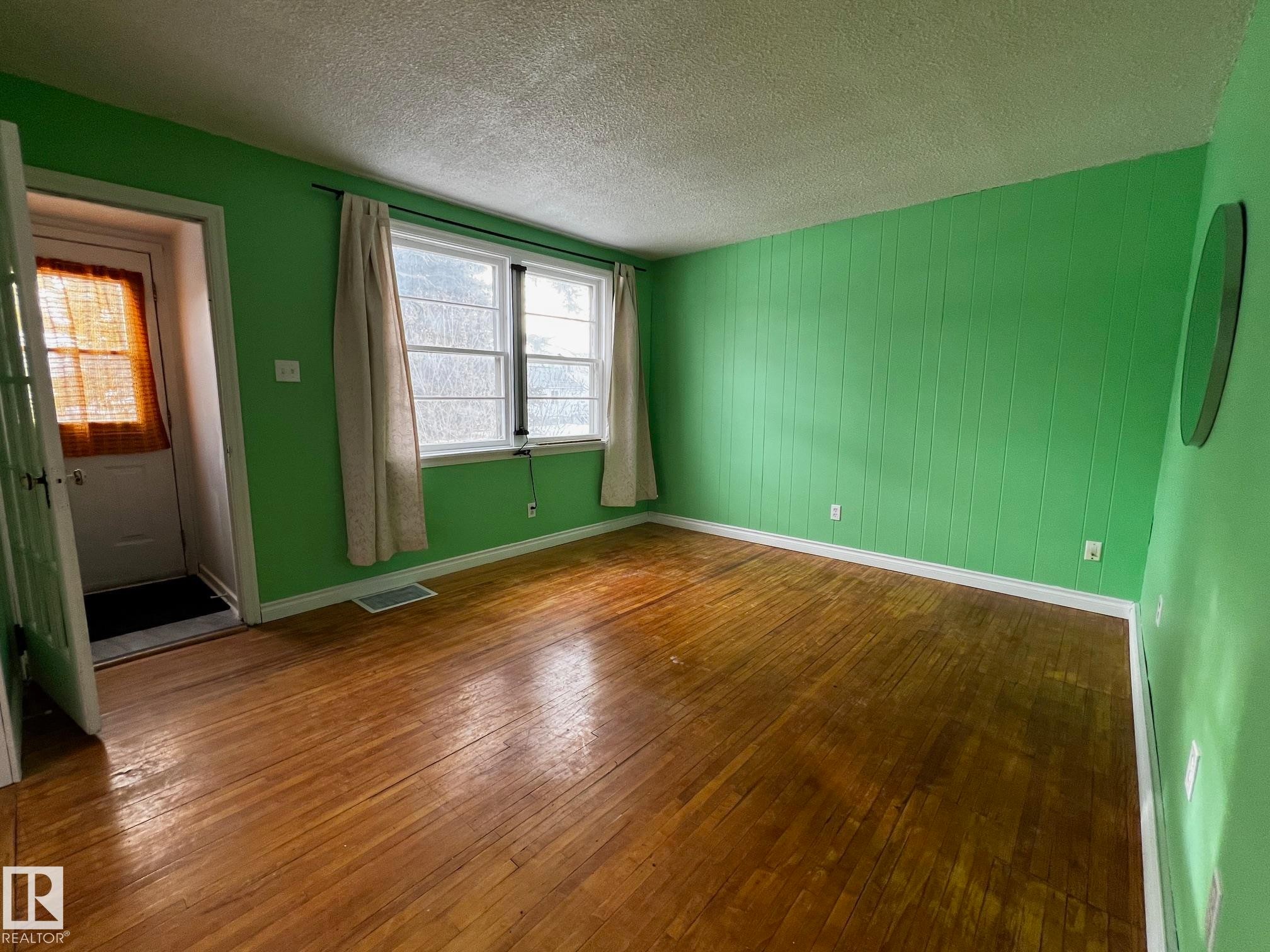 Empty room with dark wood finished floors, a textured ceiling, and wooden walls - 10830 68 Avenue, Edmonton, AB - Indoor Photo Showing Other Room