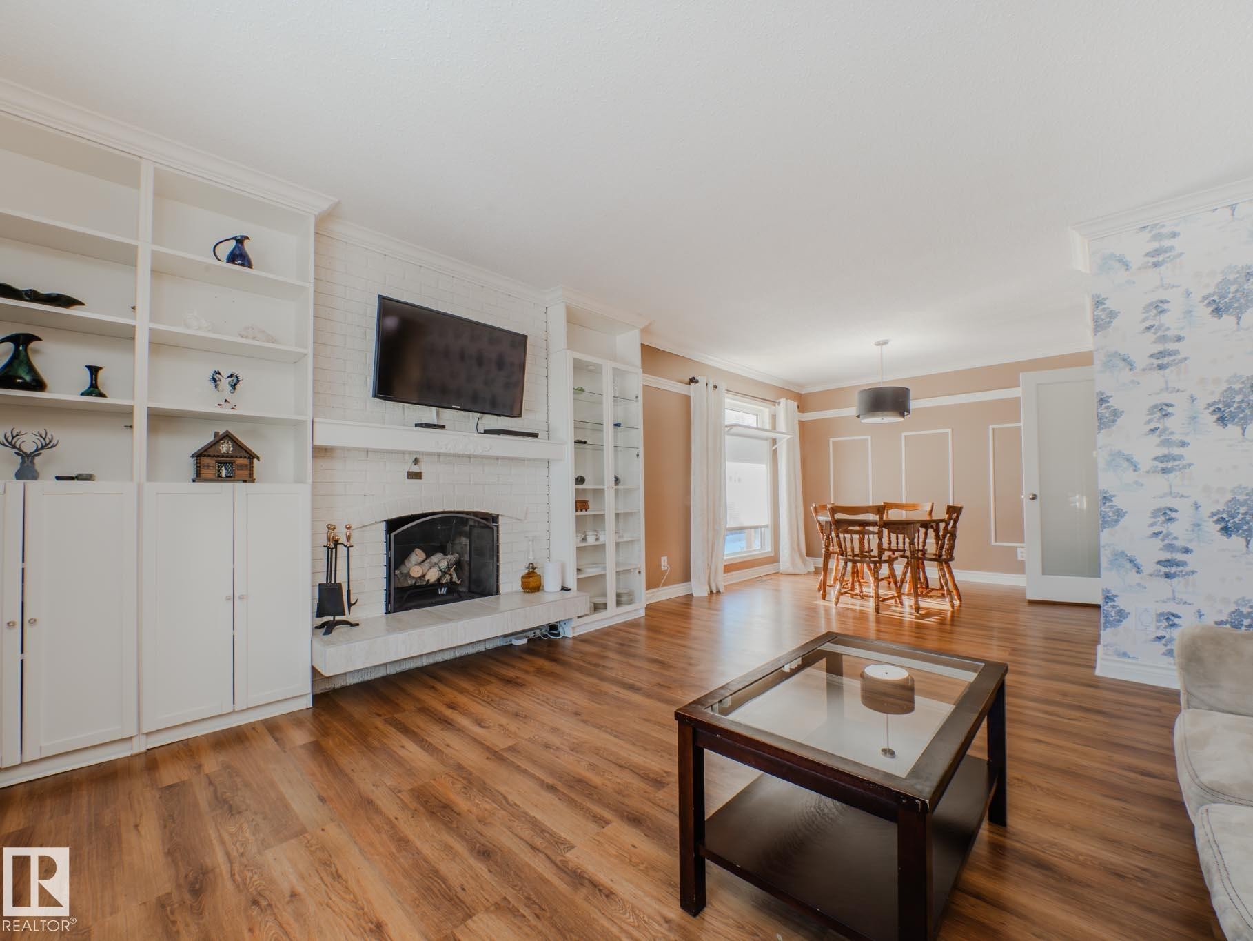 Living area featuring a brick fireplace, wood finished floors, built in shelves, and ornamental molding - 3204 113B Street, Edmonton, AB - Indoor Photo Showing Living Room With Fireplace