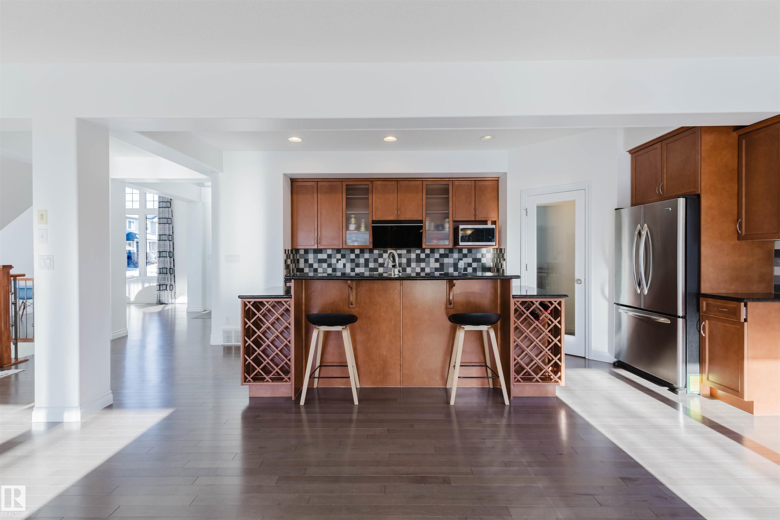 Kitchen featuring stainless steel appliances, glass fronted cabinets, a kitchen bar, dark wood-style flooring, and wood finish cabinetry - 3547 Mclay Crescent, Edmonton, AB - Indoor Photo Showing Kitchen
