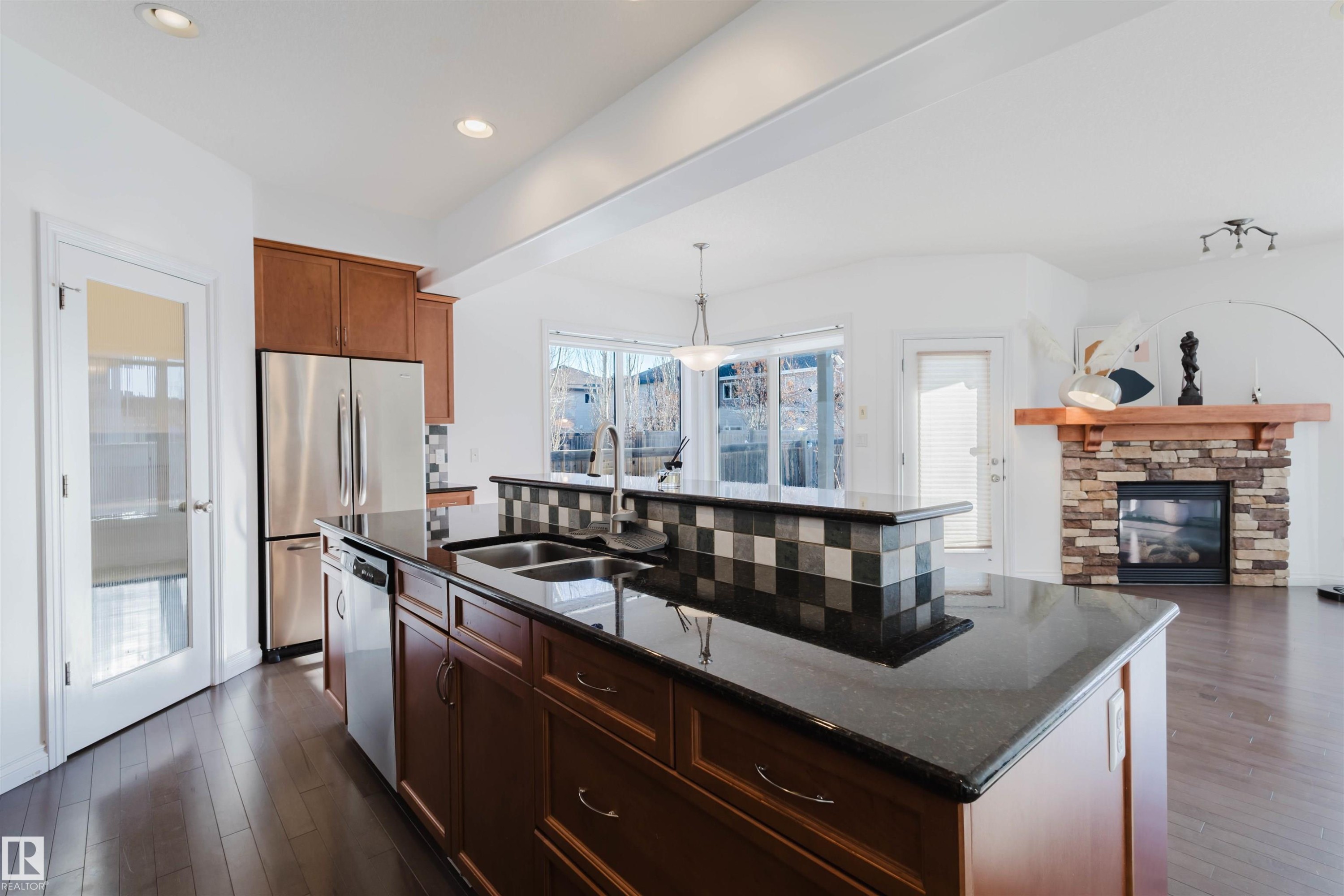 Kitchen with dark stone counters, a center island with sink, decorative light fixtures, and healthy amount of natural light - 3547 Mclay Crescent, Edmonton, AB - Indoor Photo Showing Kitchen With Fireplace With Stainless Steel Kitchen With Double Sink With Upgraded Kitchen