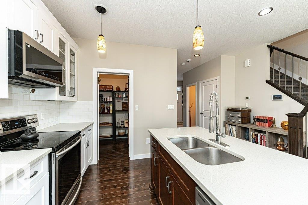 Kitchen with stainless steel appliances, hanging light fixtures, dark wood-type flooring, light stone countertops, and glass insert cabinets - 10535 67 Avenue, Edmonton, AB - Indoor Photo Showing Kitchen With Stainless Steel Kitchen With Double Sink