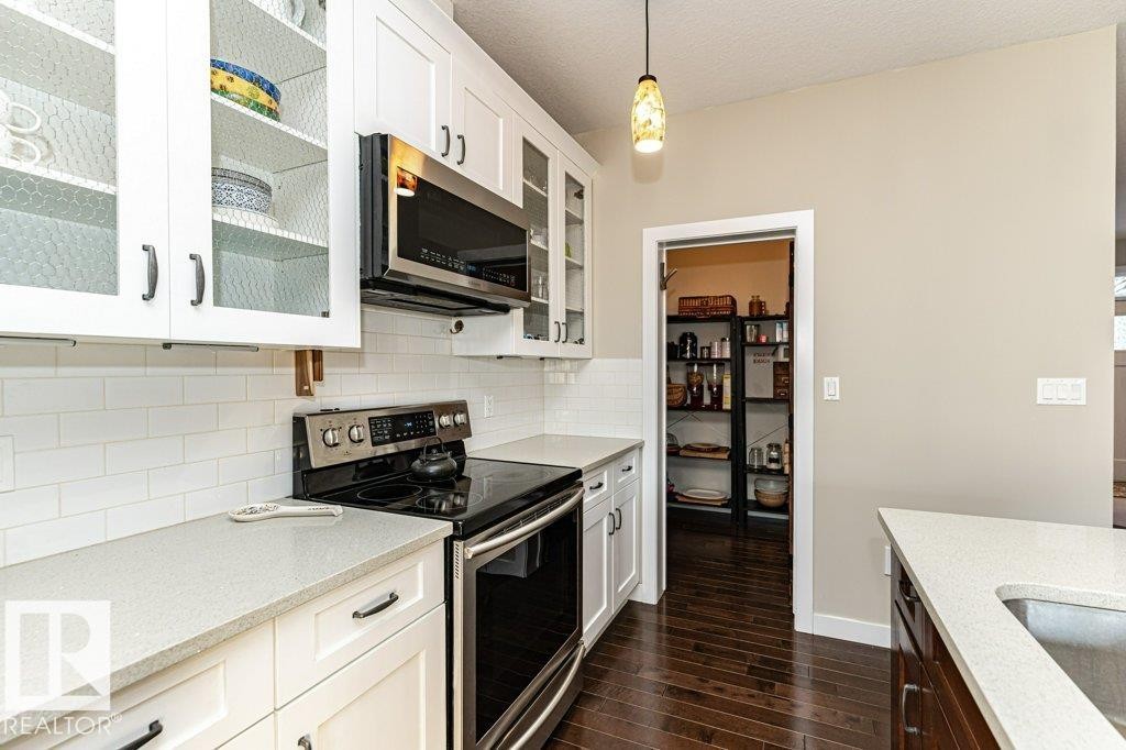Kitchen featuring stainless steel appliances, white cabinets, light stone countertops, tasteful backsplash, and dark wood-style flooring - 10535 67 Avenue, Edmonton, AB - Indoor Photo Showing Kitchen With Upgraded Kitchen