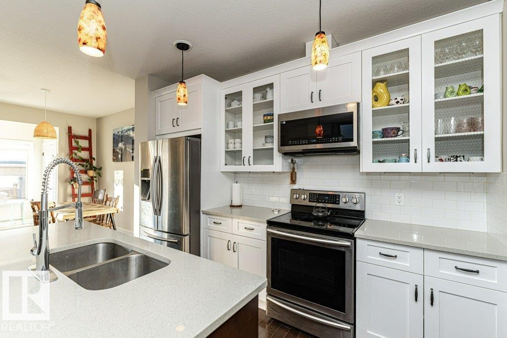 Kitchen featuring stainless steel appliances, white cabinets, pendant lighting, and light stone counters - 10535 67 Avenue, Edmonton, AB - Indoor Photo Showing Kitchen With Stainless Steel Kitchen With Double Sink