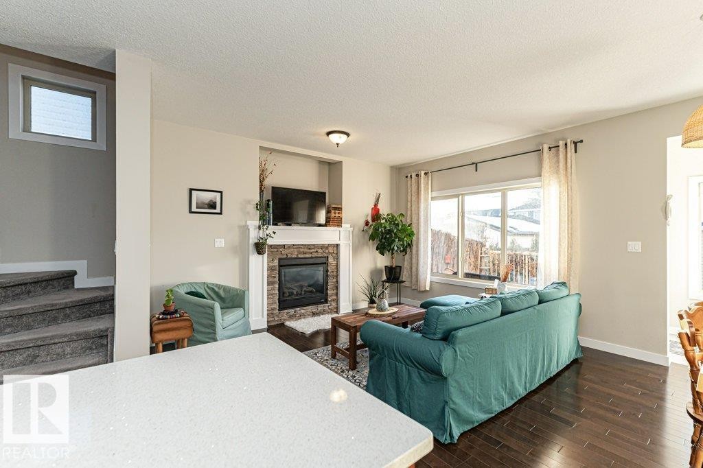 Living area featuring dark wood-type flooring, a stone fireplace, and a textured ceiling - 10535 67 Avenue, Edmonton, AB - Indoor Photo Showing Living Room With Fireplace