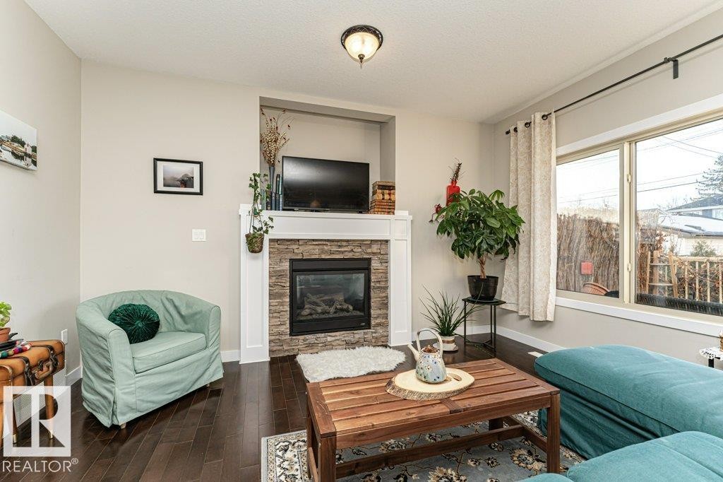 Living room with a stone fireplace, dark wood finished floors, and a textured ceiling - 10535 67 Avenue, Edmonton, AB - Indoor Photo Showing Living Room With Fireplace