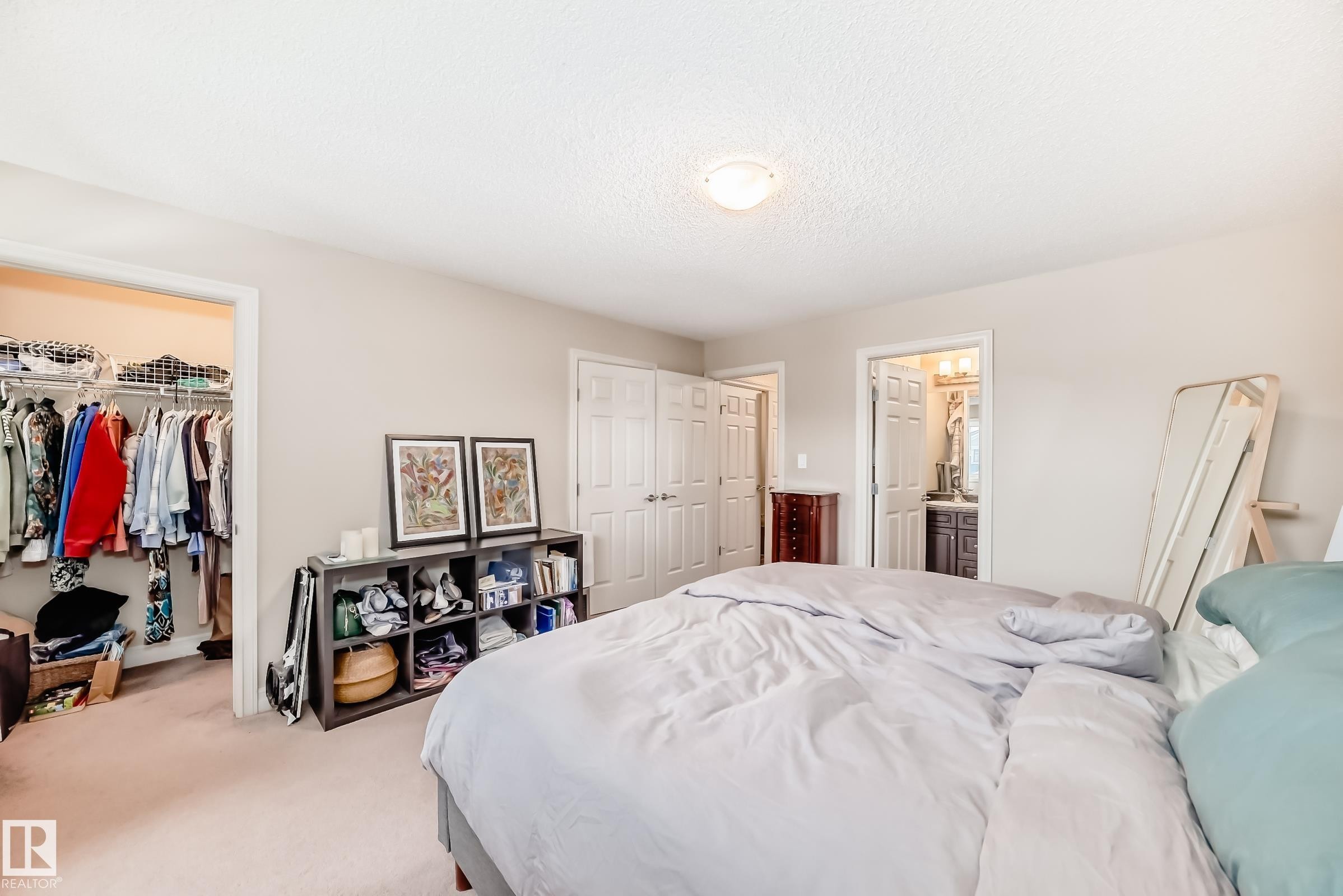 Bedroom featuring carpet floors, a textured ceiling, a spacious closet, and connected bathroom - 9645 Simpson Place, Edmonton, AB