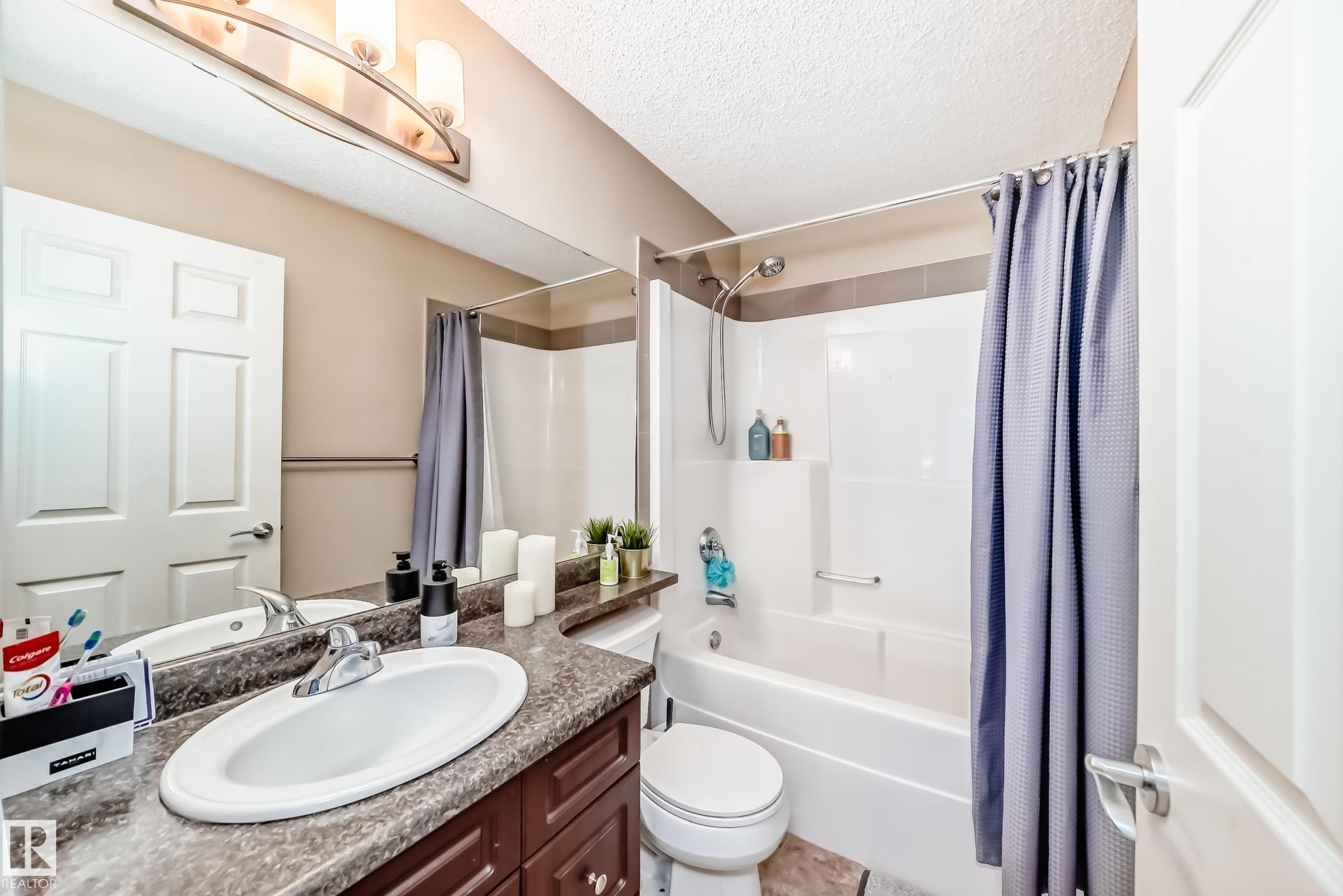 Bathroom featuring vanity, shower / bathtub combination with curtain, and a textured ceiling - 9645 Simpson Place, Edmonton, AB