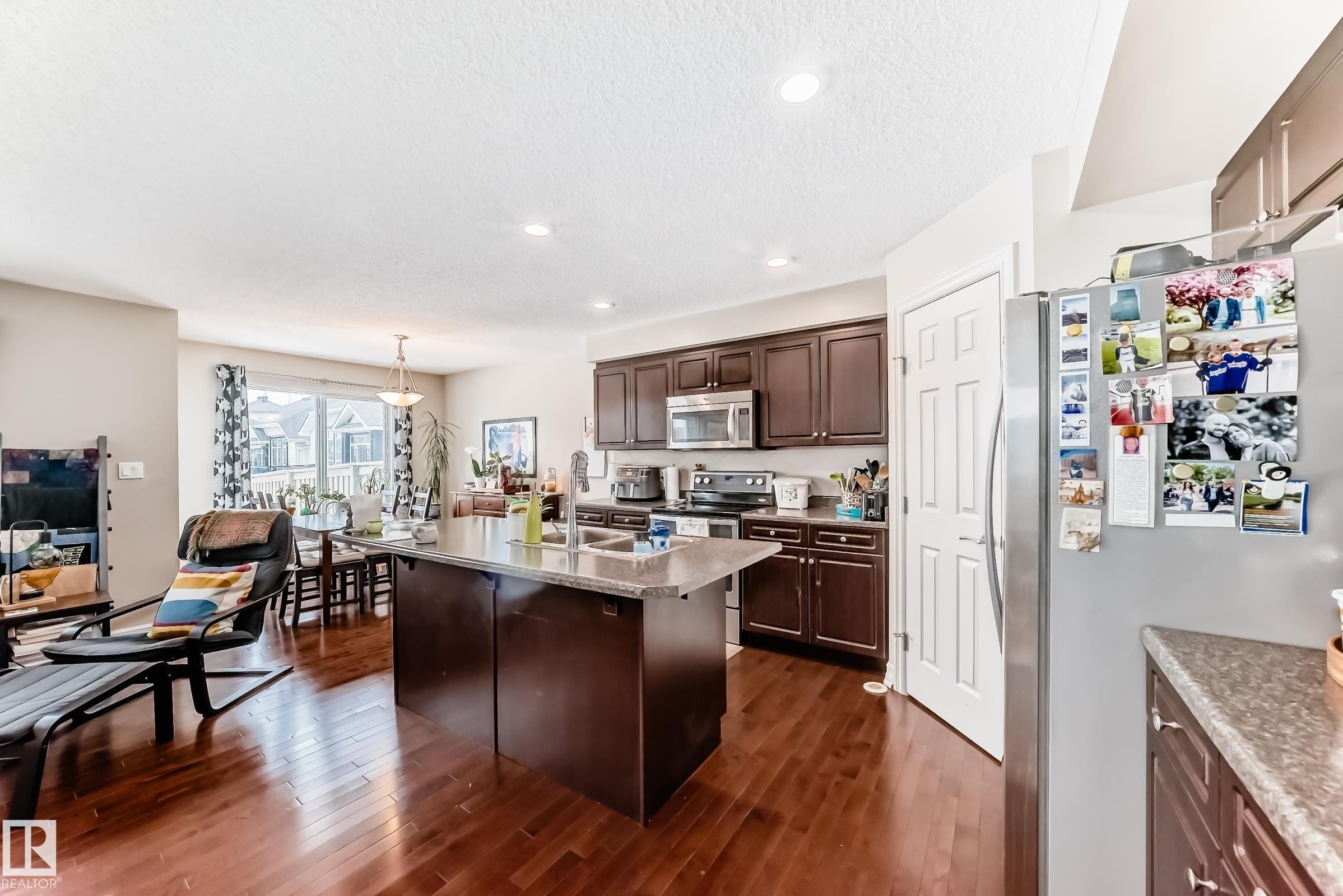 Kitchen featuring stainless steel appliances, dark wood finish cabinets, a kitchen island with sink, pendant lighting, and dark wood-type flooring - 9645 Simpson Place, Edmonton, AB