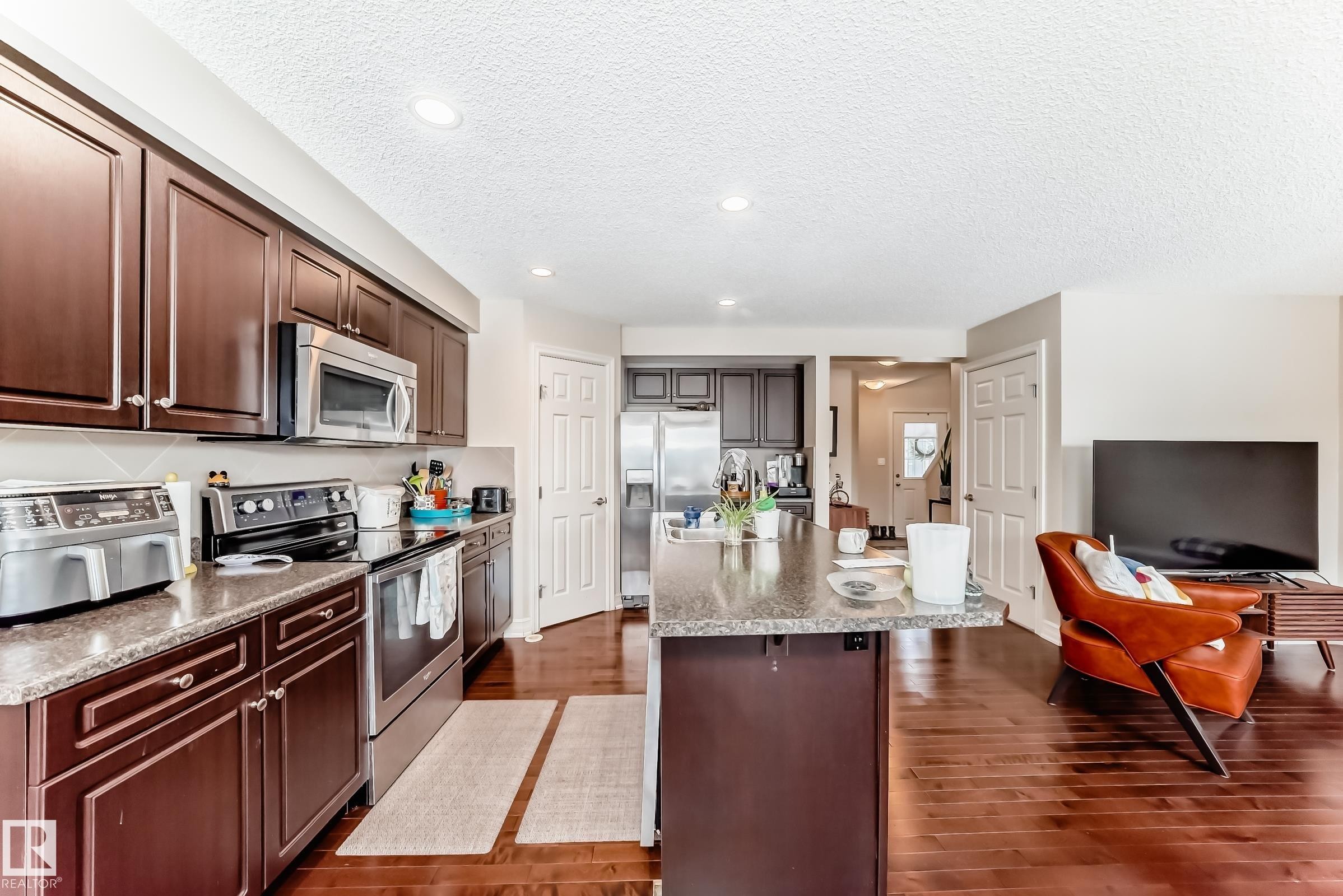 Kitchen featuring stainless steel appliances, dark wood finish cabinets, a textured ceiling, dark wood-style flooring, and a breakfast bar area - 9645 Simpson Place, Edmonton, AB