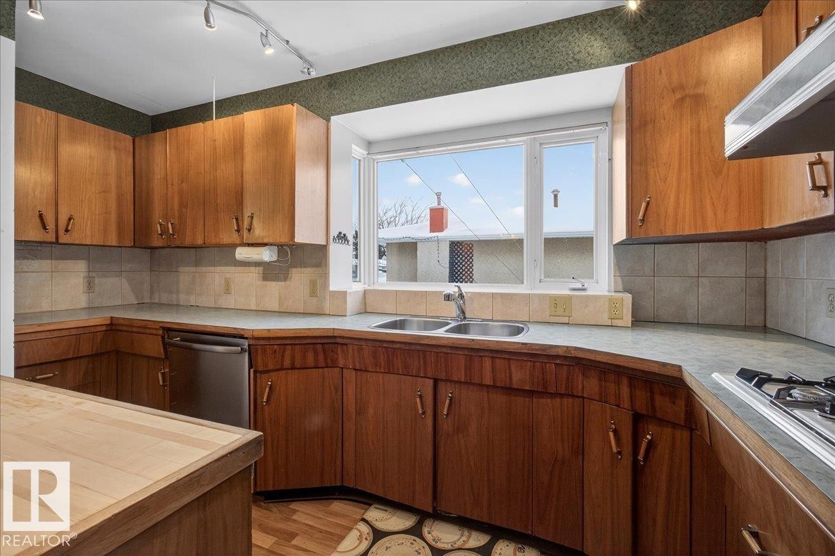 Kitchen featuring wood finish cabinetry, decorative backsplash, light countertops, and stainless steel appliances - Edmonton, AB - Indoor Photo Showing Kitchen With Double Sink