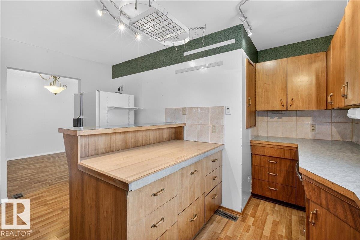Kitchen with light countertops, wood finish cabinets, decorative backsplash, light wood-style floors, and rail lighting - Edmonton, AB - Indoor Photo Showing Kitchen