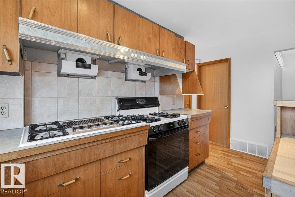 Kitchen featuring gas range oven, wood finish cabinetry, light countertops, and backsplash - Edmonton, AB - Indoor Photo Showing Kitchen