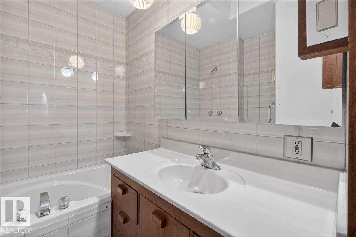 Full bath with tile walls, vanity, a bathtub, and a shower - Edmonton, AB - Indoor Photo Showing Bathroom