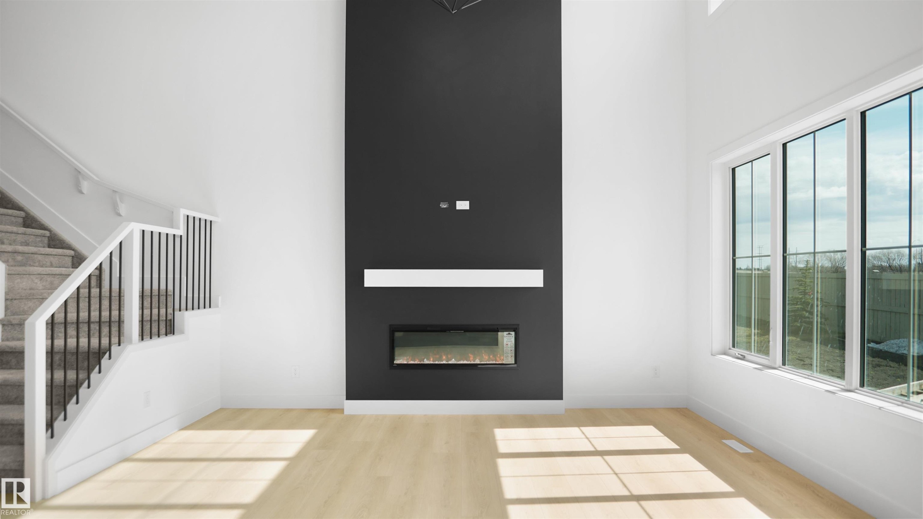 Unfurnished living room featuring a towering ceiling, stairs, light wood-style floors, and a glass covered fireplace - 807 30 Avenue, Edmonton, AB - Indoor With Fireplace