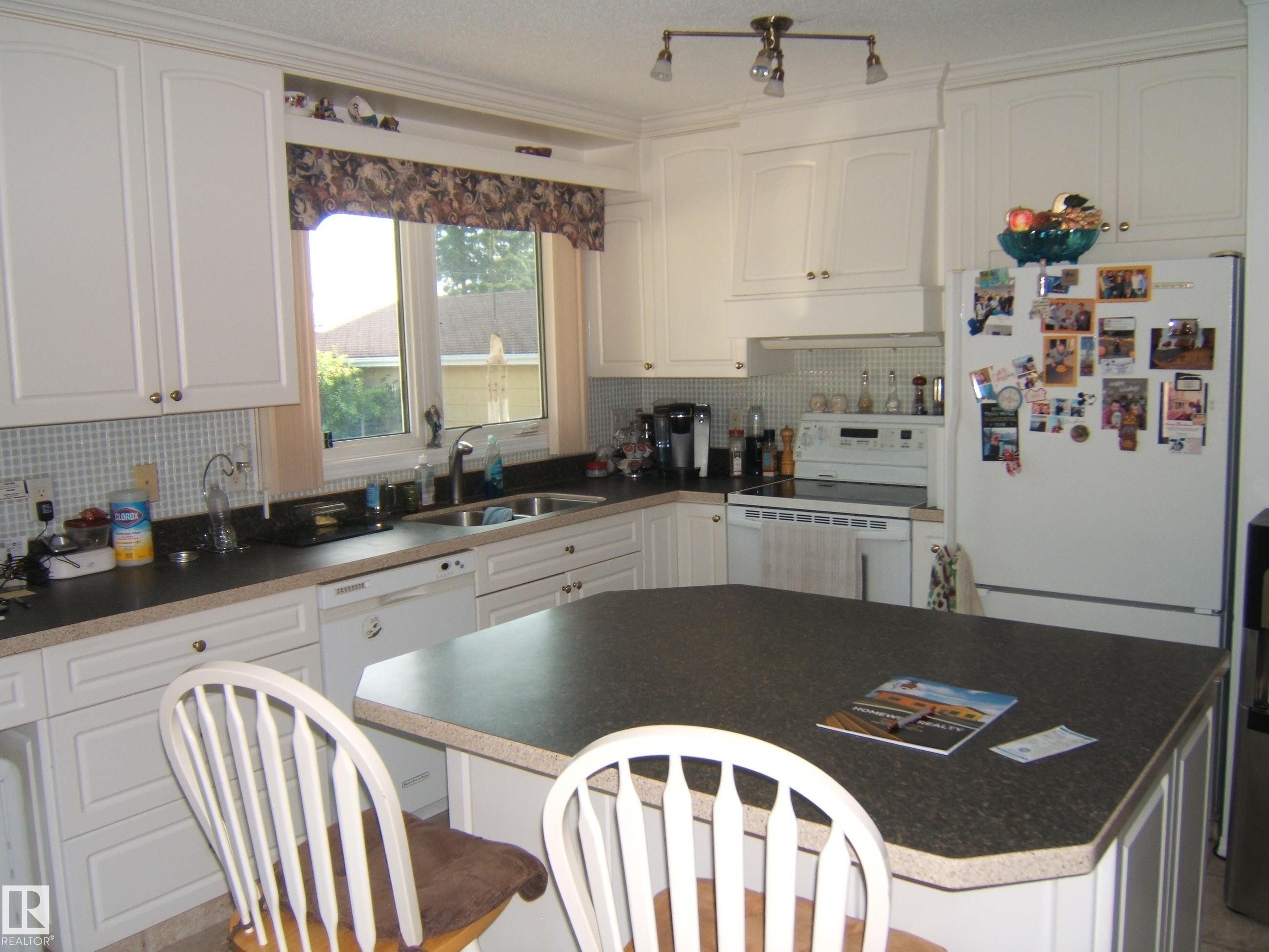 Kitchen featuring white appliances, white cabinets, tasteful backsplash, a kitchen bar, and a center island - 4807 54 Avenue, Two Hills, AB - Indoor Photo Showing Kitchen With Double Sink