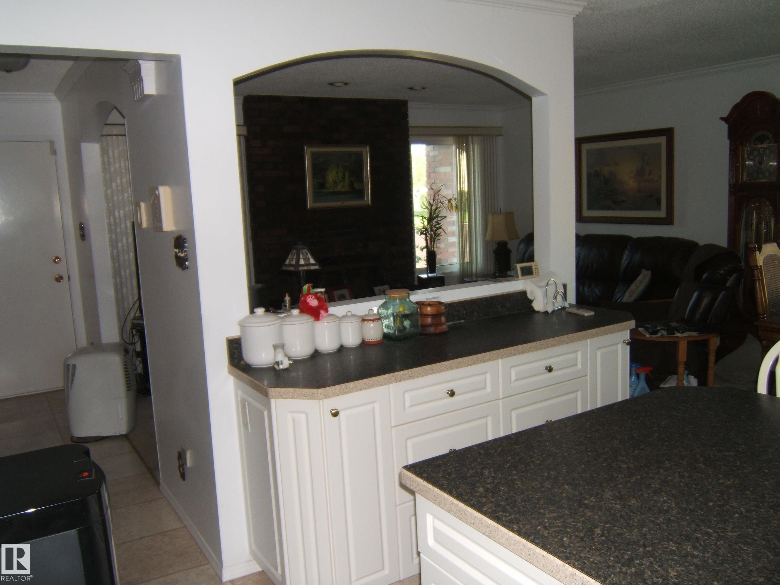 Kitchen with crown molding, dark countertops, white cabinets, light tile patterned floors, and open floor plan - 4807 54 Avenue, Two Hills, AB - Indoor
