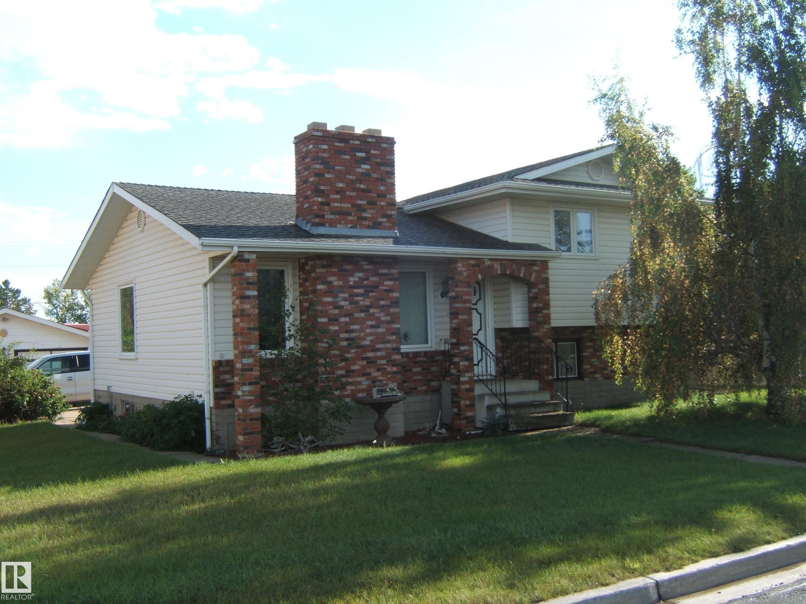 View of front of home featuring a chimney, a front yard, brick siding, and roof with shingles - 4807 54 Avenue, Two Hills, AB - Outdoor