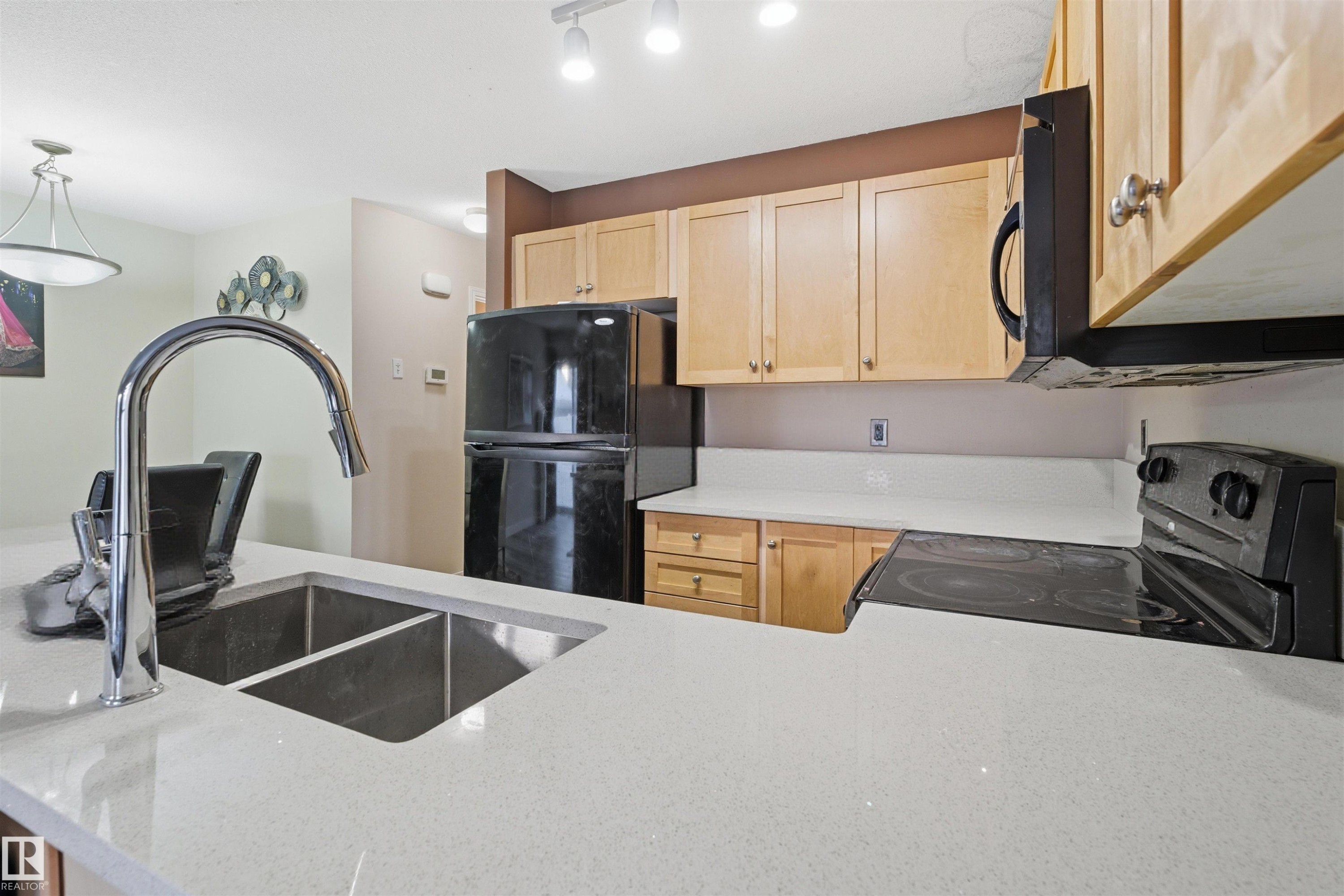 Kitchen featuring light wood finish cabinets, black appliances, light stone counters, and pendant lighting - 8 230 Edwards Drive, Edmonton, AB - Indoor Photo Showing Kitchen With Double Sink