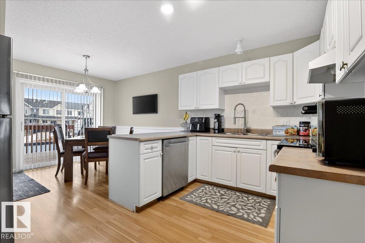 Kitchen with a peninsula, backsplash, white cabinets, black appliances, and light wood-style flooring - 13217 155 Avenue Nw, Edmonton, AB - Indoor Photo Showing Kitchen