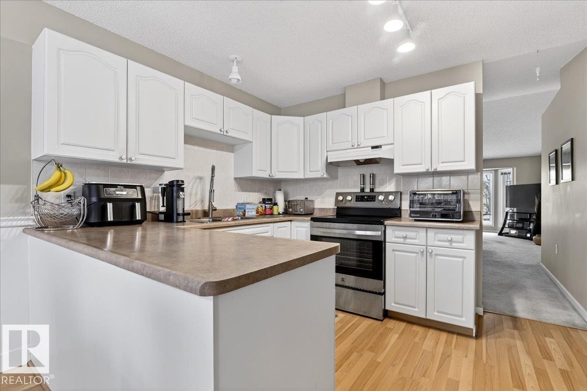 Kitchen featuring stainless steel range with electric cooktop, white cabinetry, a peninsula, a textured ceiling, and tasteful backsplash - 13217 155 Avenue Nw, Edmonton, AB - Indoor Photo Showing Kitchen With Double Sink