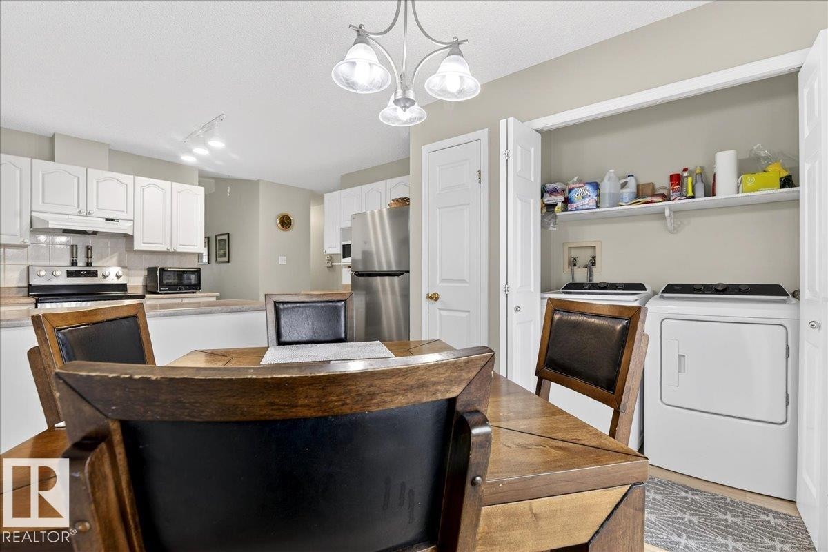 Kitchen with white cabinetry, light countertops, stainless steel appliances, washing machine and clothes dryer, and a chandelier - 13217 155 Avenue Nw, Edmonton, AB - Indoor Photo Showing Laundry Room