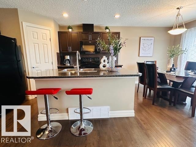 Kitchen featuring a kitchen island with sink, black appliances, a kitchen breakfast bar, dark wood-type flooring, and pendant lighting - 12219 167A Avenue, Edmonton, AB - Indoor