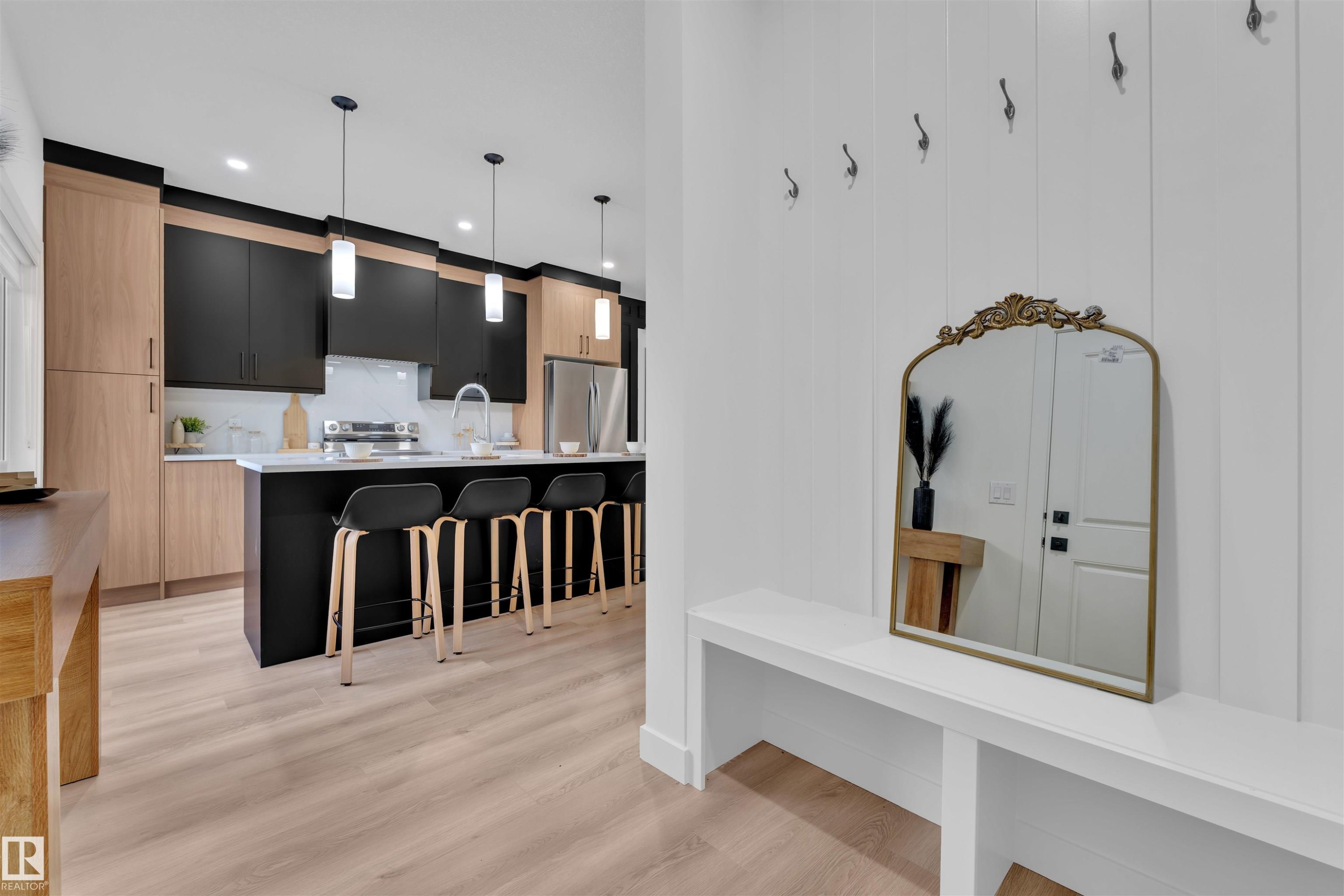 Kitchen with dark cabinetry, light brown cabinetry, a kitchen breakfast bar, a center island with sink, and decorative light fixtures - 303 Falcon Crescent, Leduc, AB - Indoor Photo Showing Kitchen