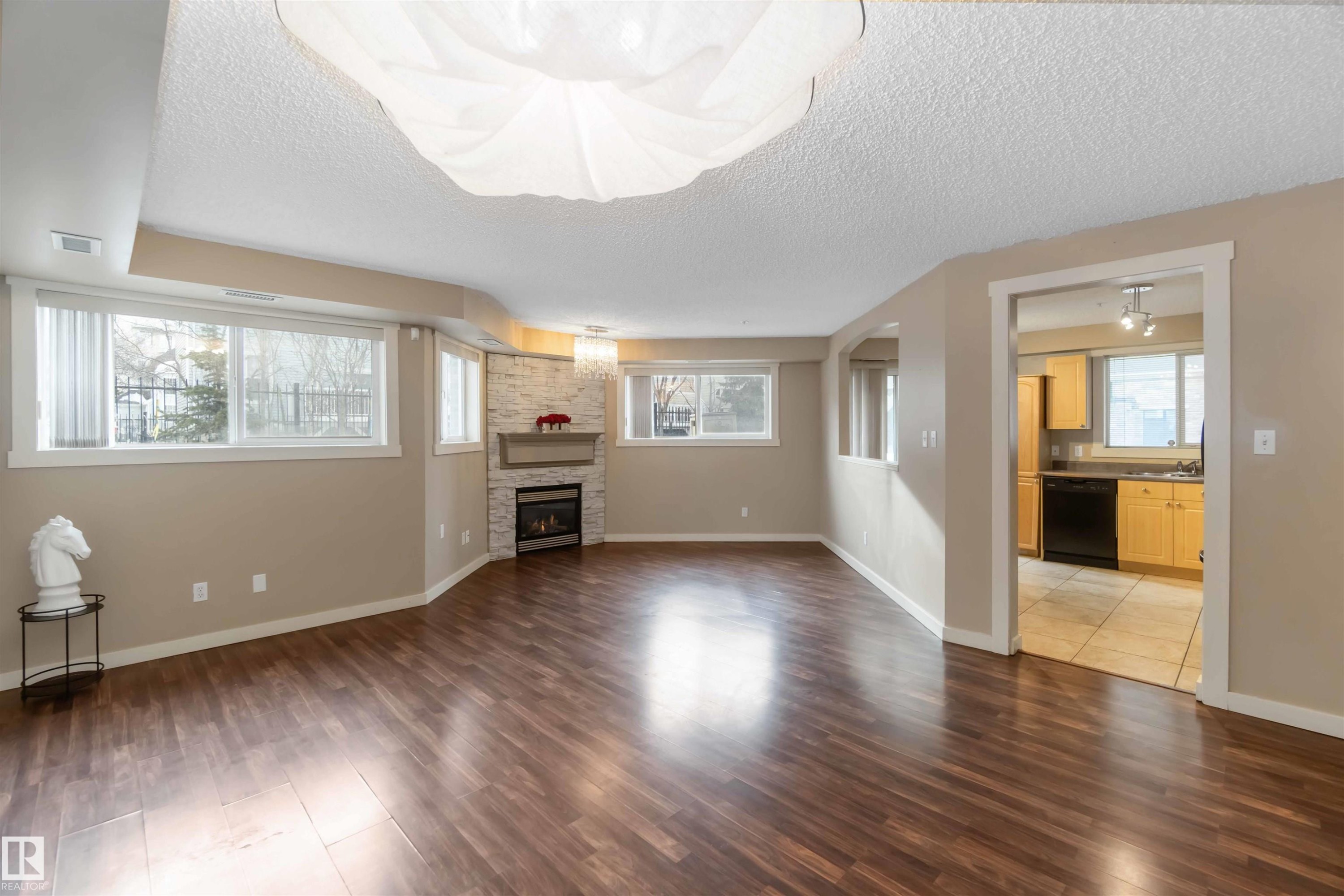 Unfurnished living room with dark wood-type flooring, a textured ceiling, and a stone fireplace - 113 10311 111 Street, Edmonton, AB - Indoor Photo Showing Other Room With Fireplace