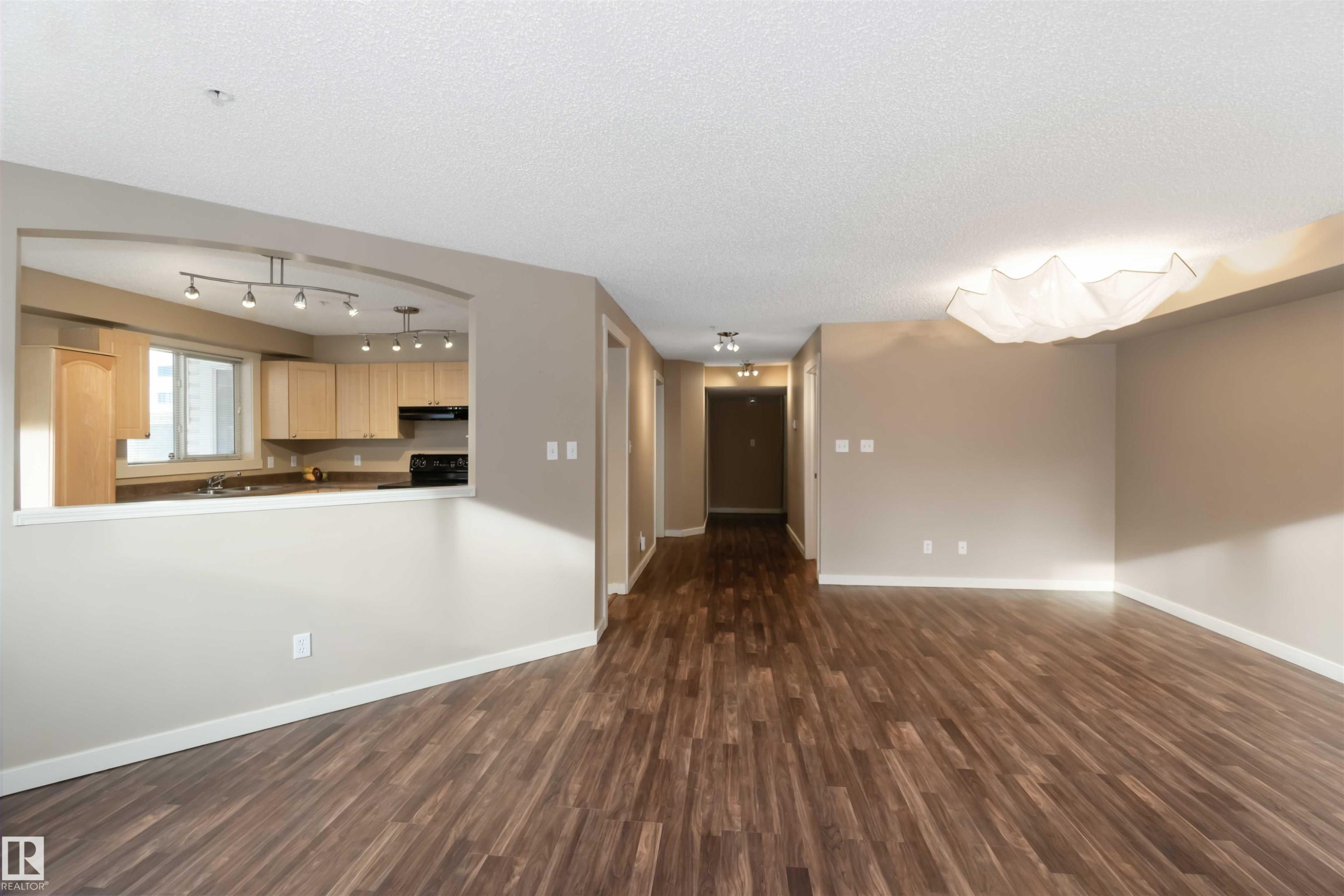 Unfurnished living room with dark wood finished floors and a textured ceiling - 113 10311 111 Street, Edmonton, AB - Indoor