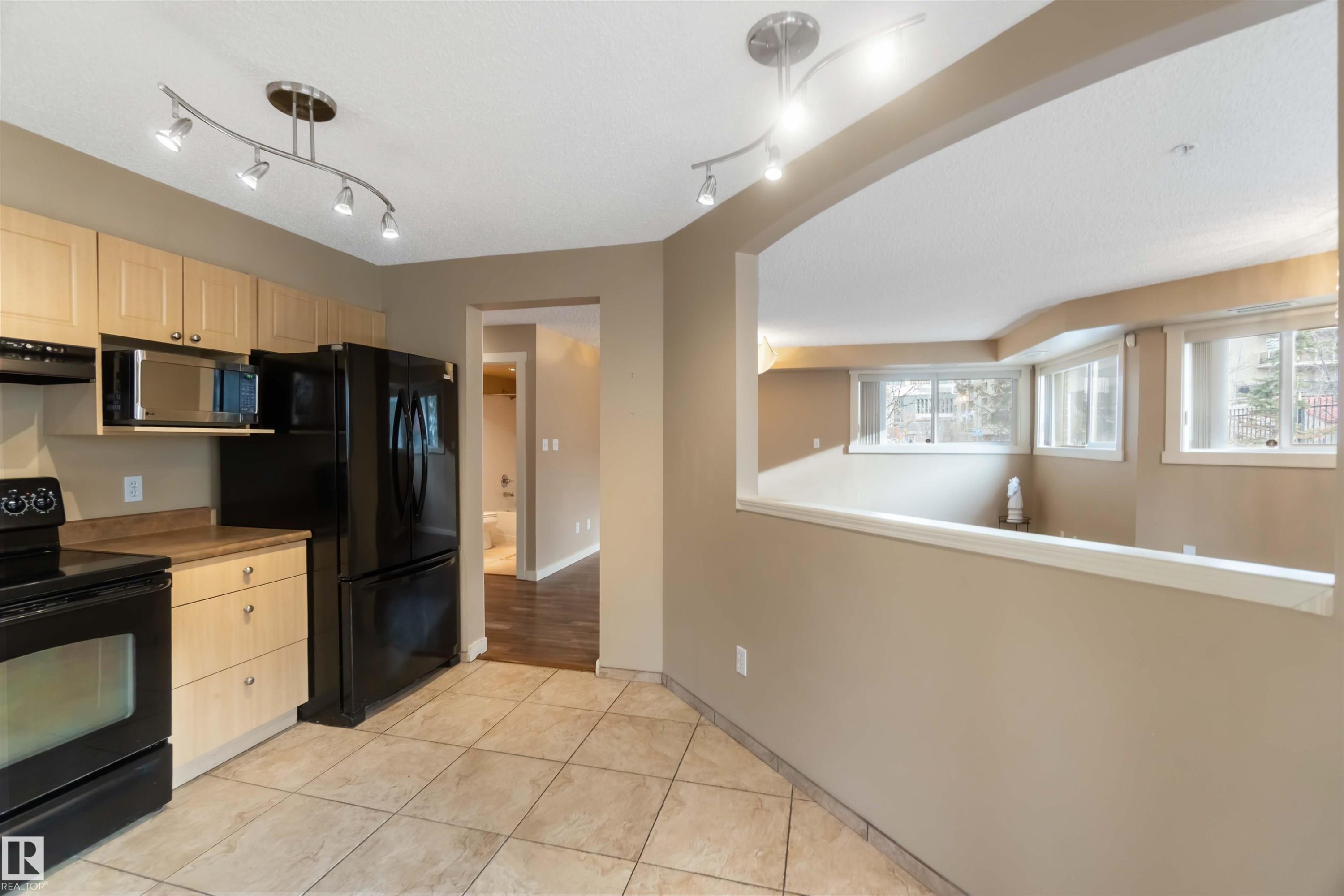 Kitchen featuring light wood finish cabinets, black appliances, light tile patterned floors, and rail lighting - 113 10311 111 Street, Edmonton, AB - Indoor Photo Showing Kitchen